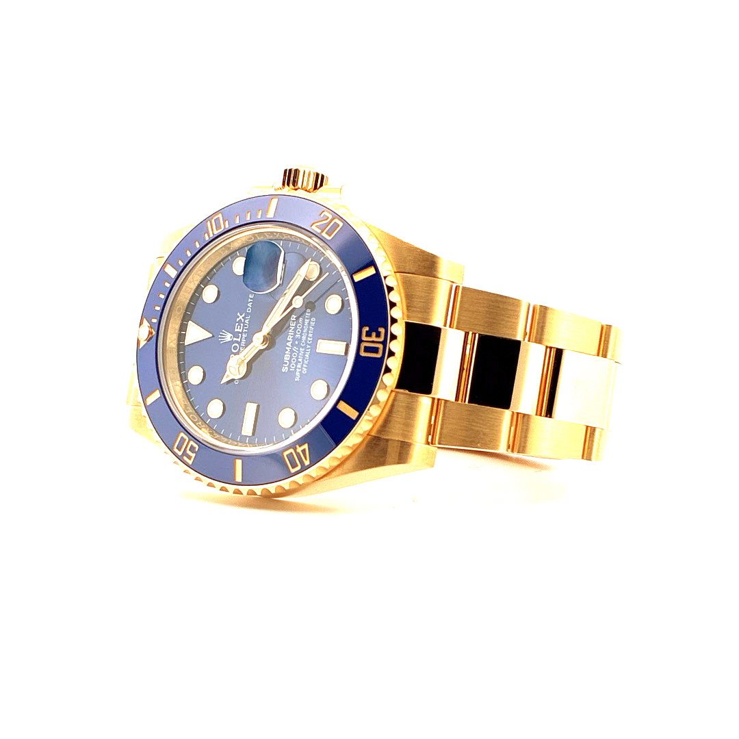 Rolex Submariner 126618LB Date Gelbgold, Perspektive leicht von oben, blaue Lünette, goldene Armbandteile auf weißem Hinte…