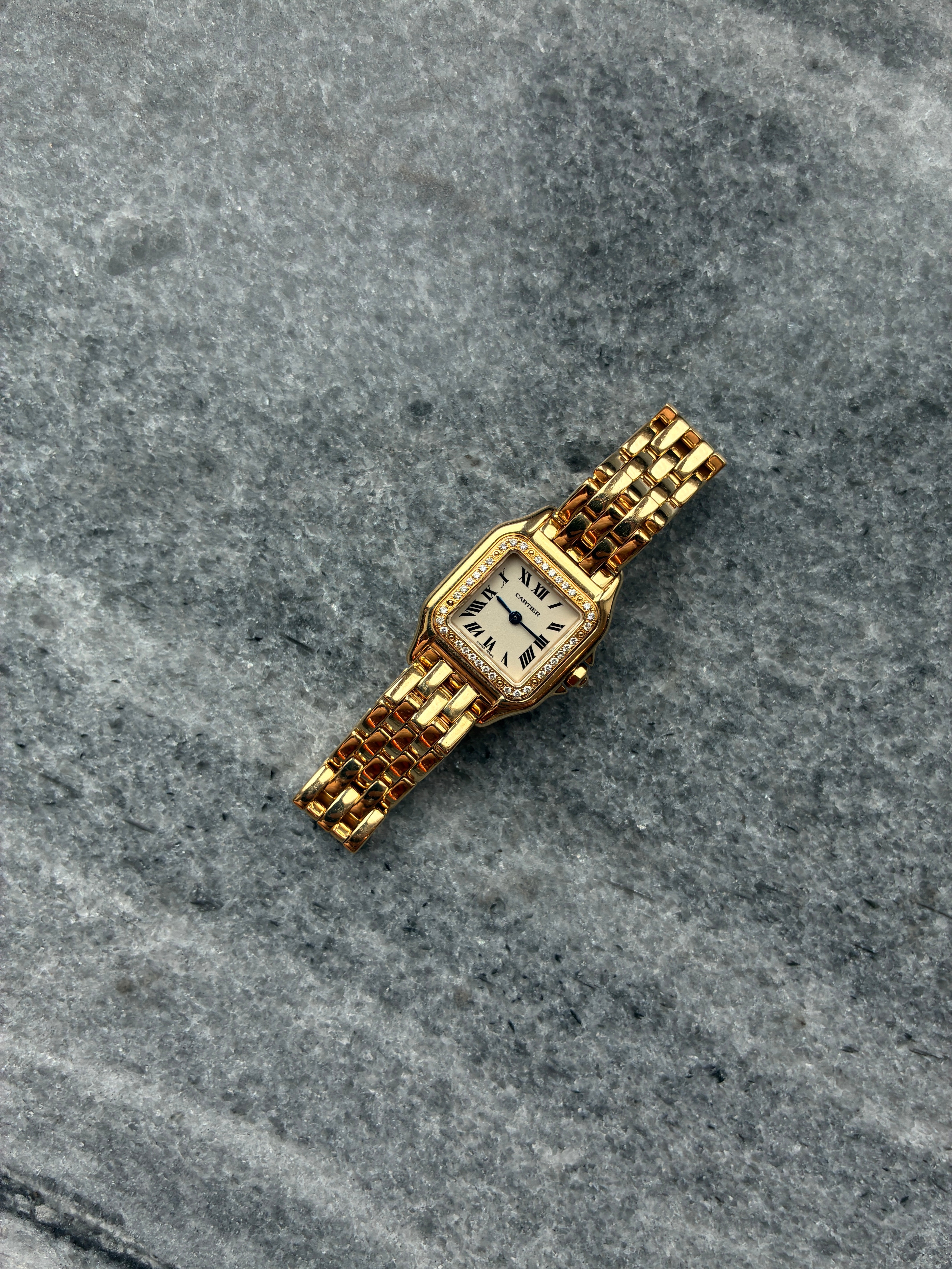 Eine Cartier Panthere 22mm Gelbgolduhr mit 32 Diamanten und römischen Ziffern auf einem grauen Marmoruntergrund
