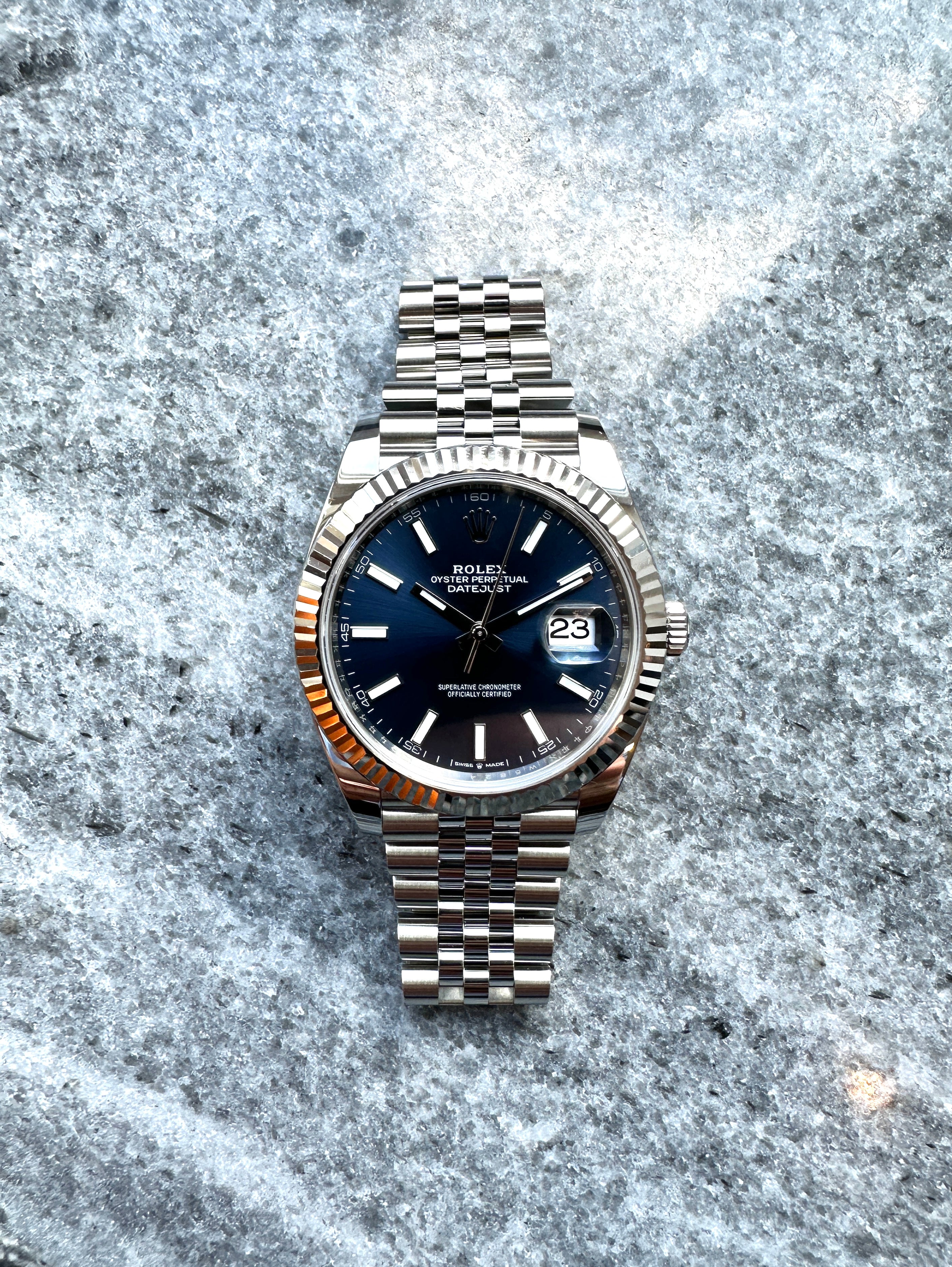 Rolex Datejust 41 mit blauem Zifferblatt und Jubilee-Armband liegt auf einem grauen Untergrund