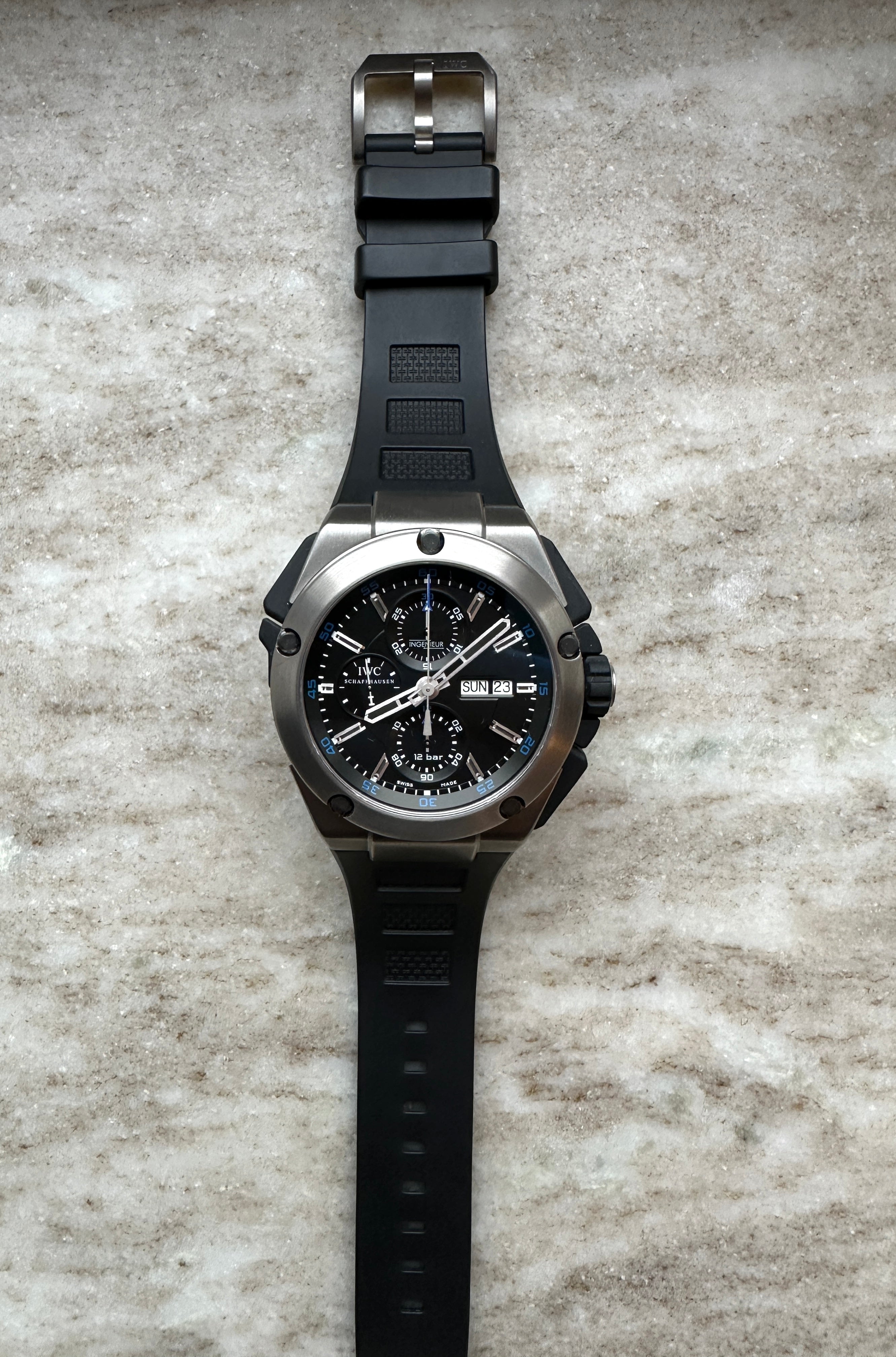 IWC Ingenieur Double Chronograph Titan mit schwarzem Zifferblatt und schwarzem Kautschukband auf hellem Untergrund