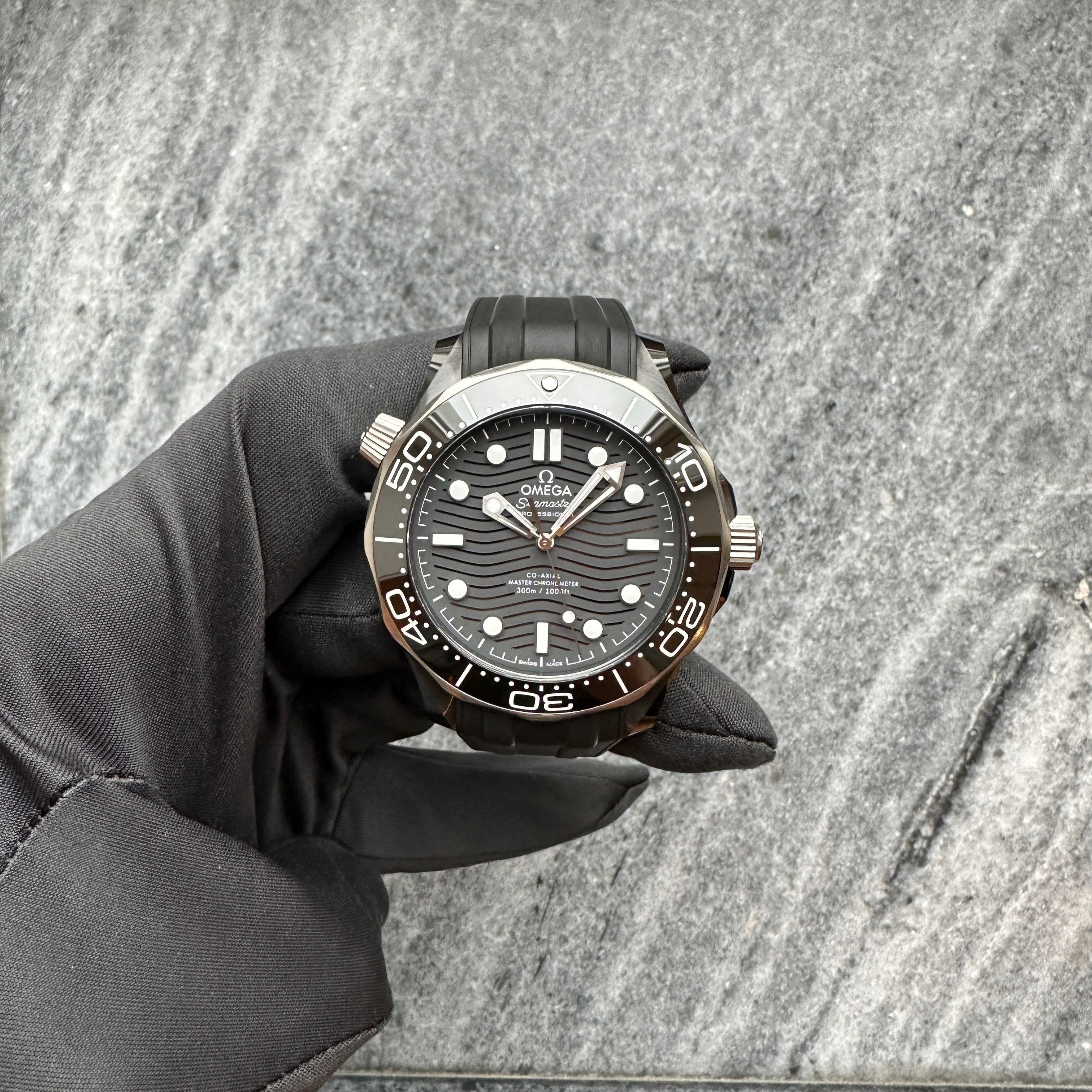 Omega Seamaster Diver 300 M mit schwarzem Zifferblatt und Kautschukband wird von einer Hand in schwarzem Handschuh gehalten