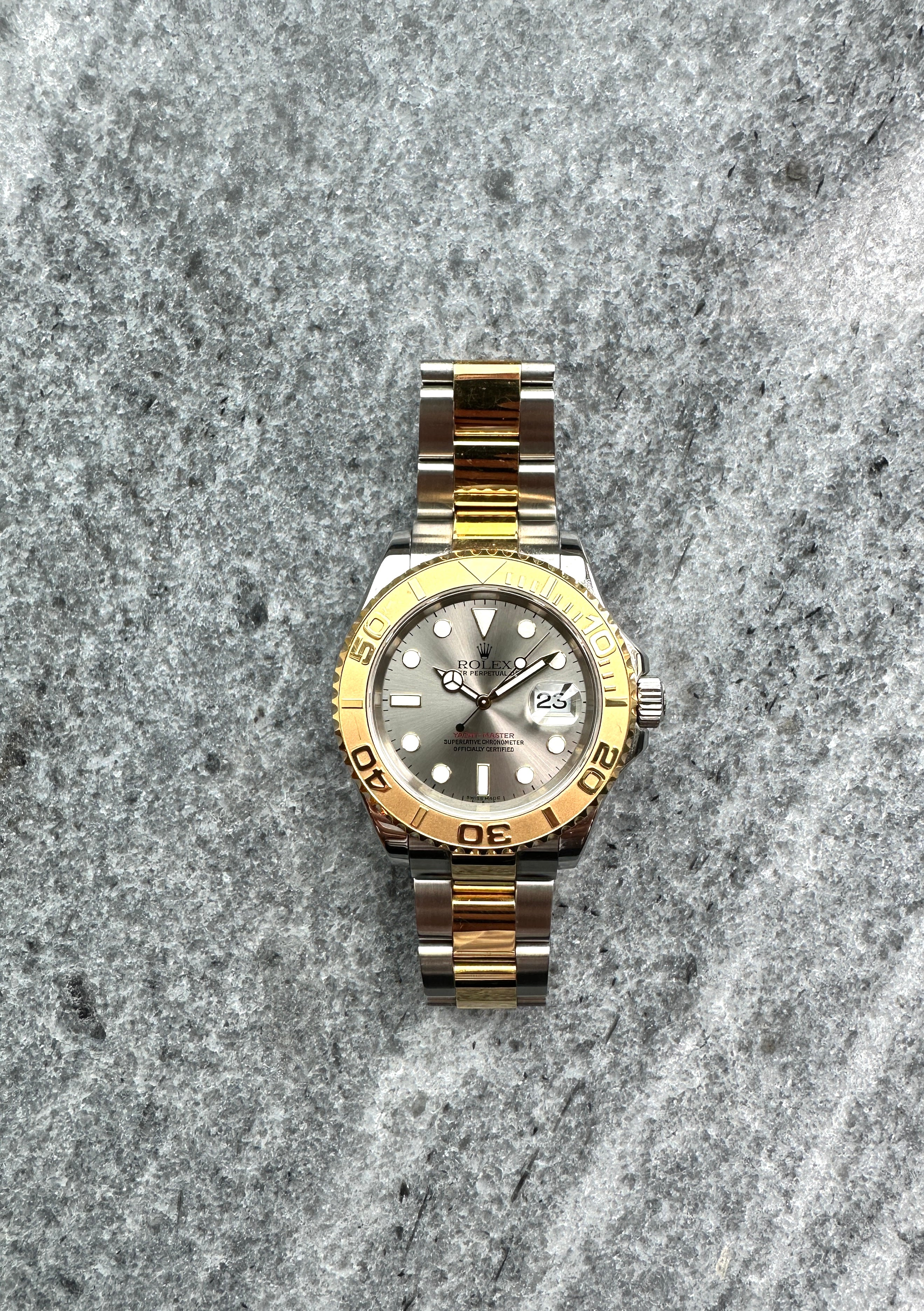 Rolex Yacht-Master 16623 mit Edelstahl und Gelbgold Gehäuse und silbernem Zifferblatt auf grauem Steinboden