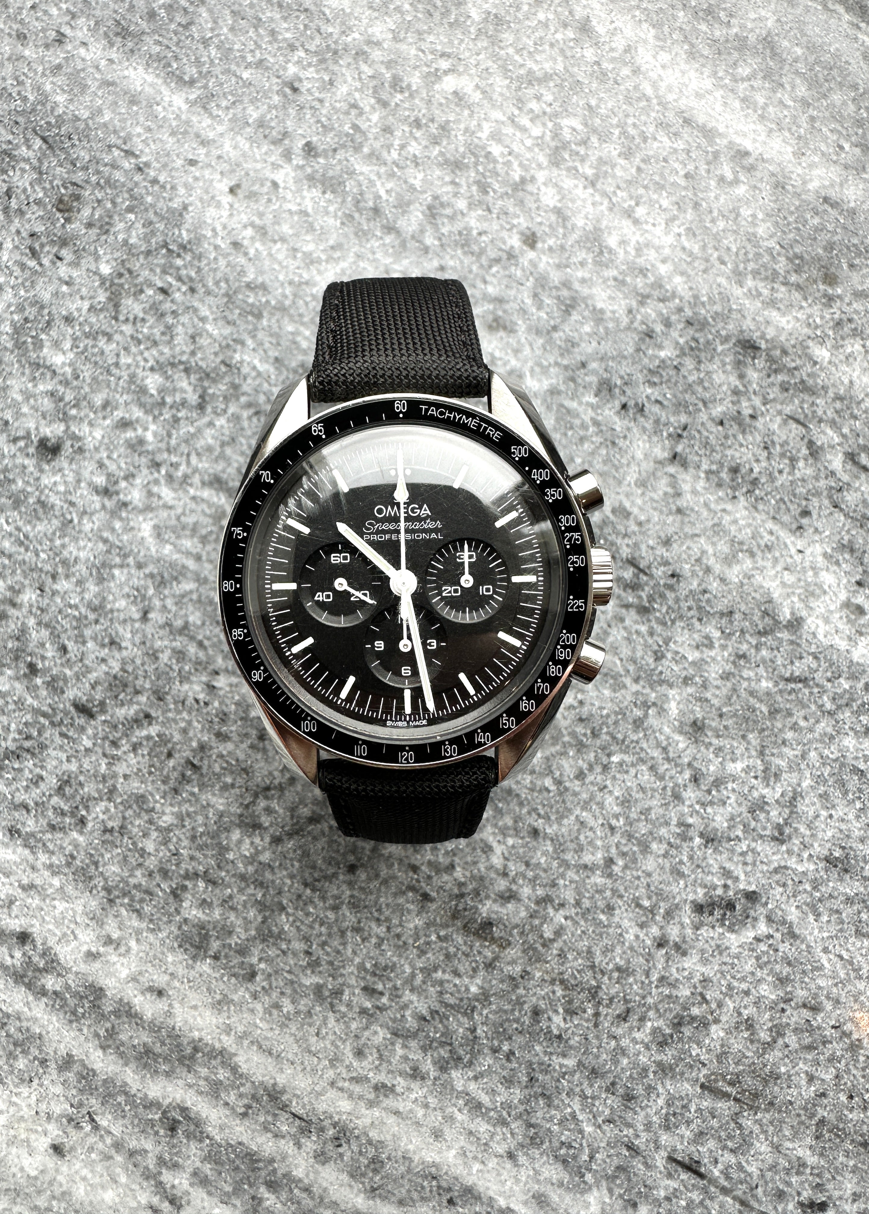 Omega Speedmaster Moonwatch Hesalit mit schwarzem Nylonband auf grauem Steinuntergrund
