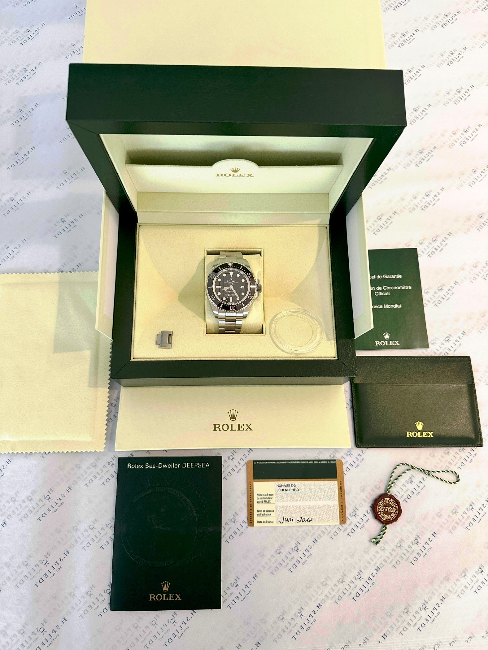 Rolex Sea-Dweller Deepsea im geöffneten Kasten mit Papieren und Siegel auf Hintergrundpapier