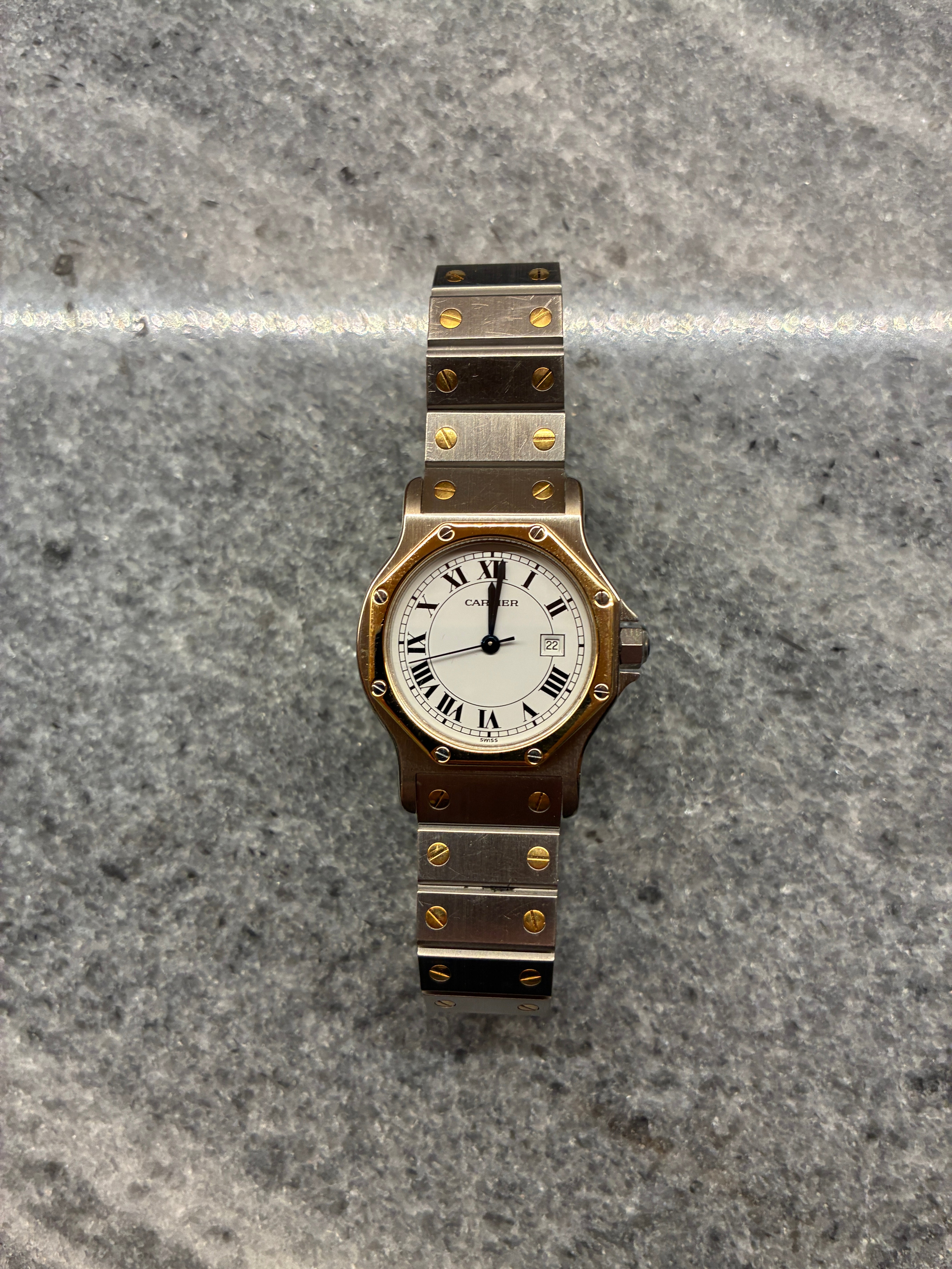 Eine Cartier Santos Octagon bicolor Uhr mit weißem Zifferblatt und römischen Ziffern auf Granithintergrund