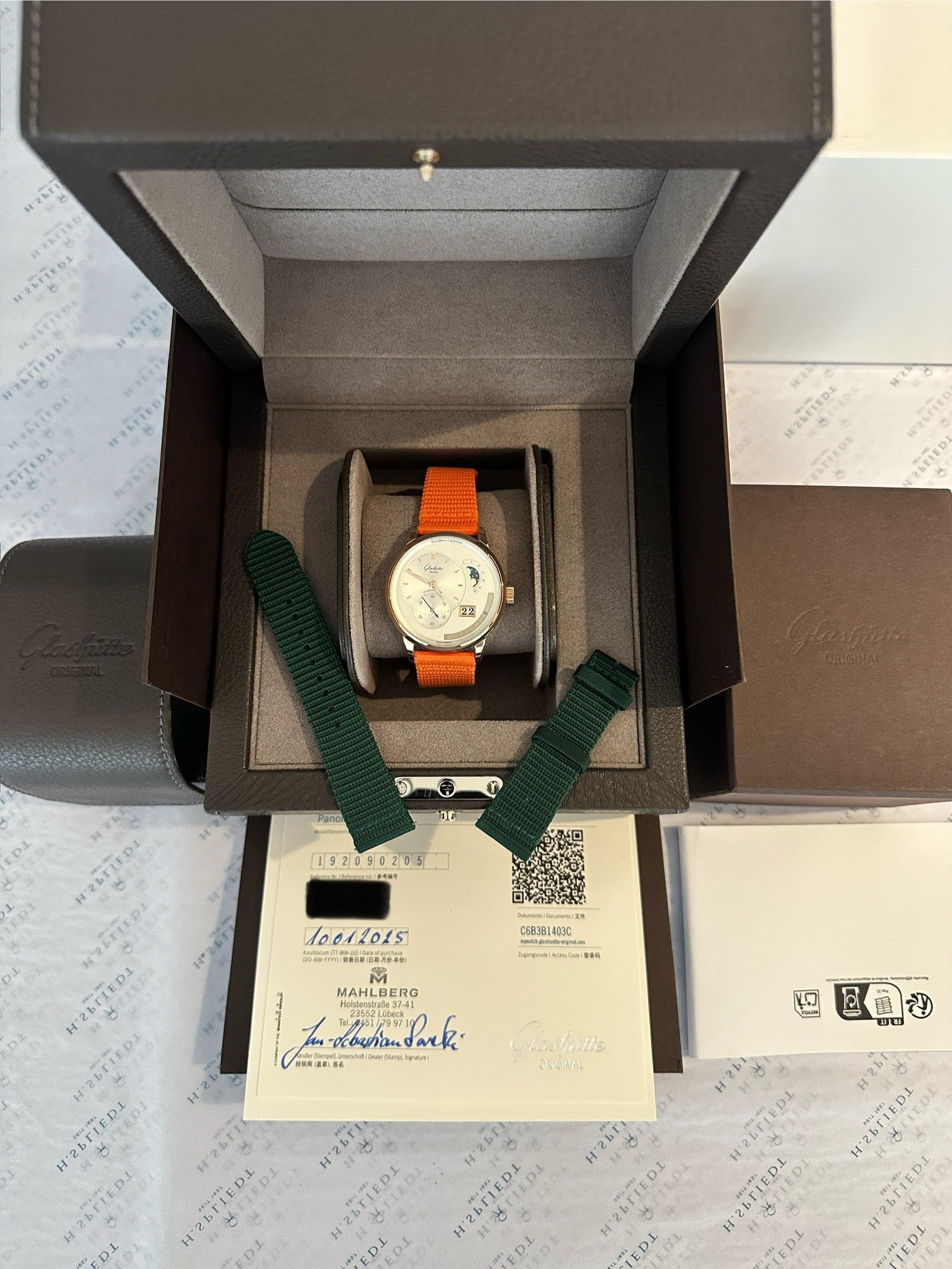 Glashütte Original Panomaticcalendar Roségold mit orangefarbenem Band und Zertifikaten im geöffneten Karton