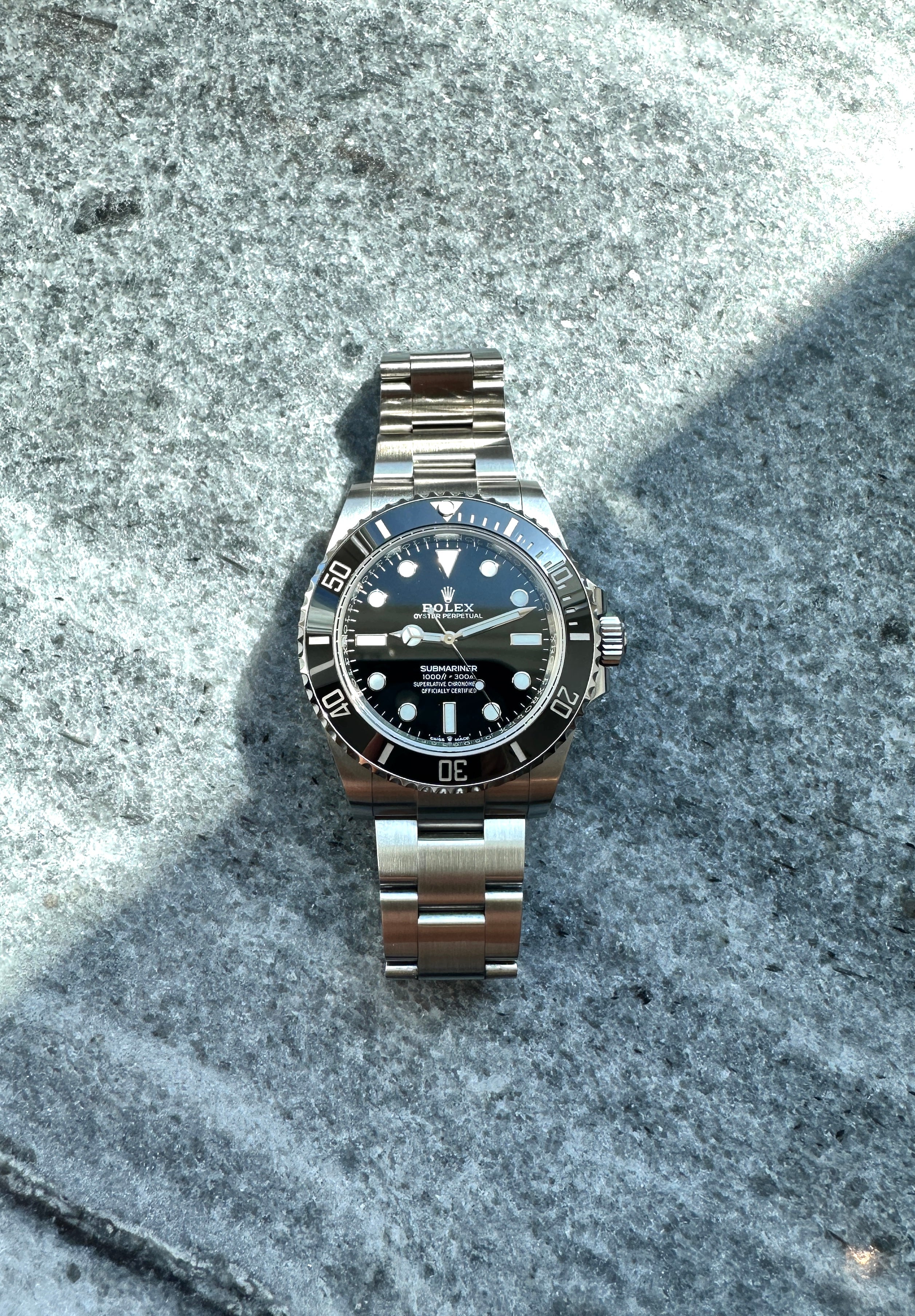 Rolex Submariner No Date aus Stahl, Frontansicht auf steinigem Untergrund, detailliert im Sonnenlicht