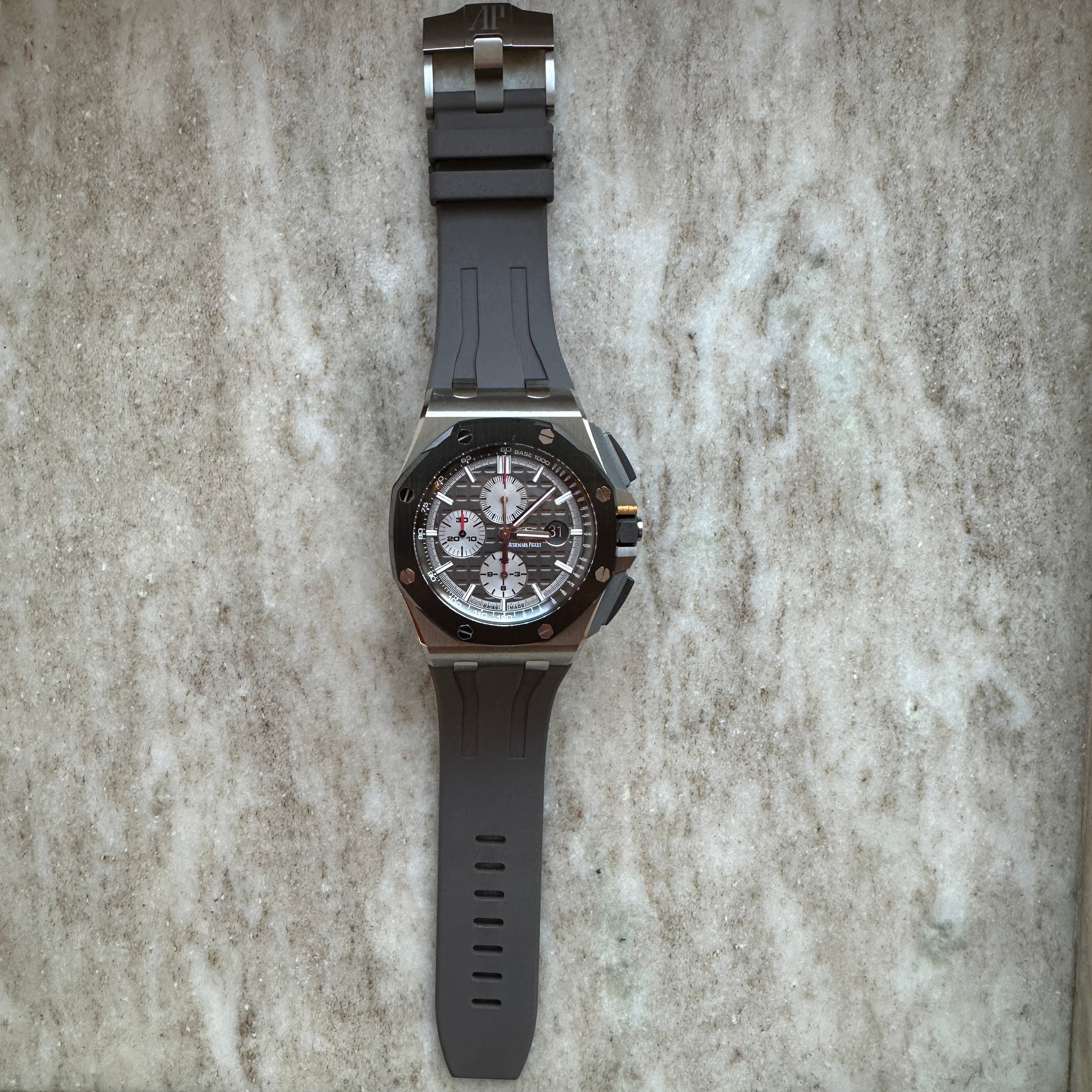 Audemars Piguet Royal Oak Offshore mit Titan Gehaeuse, grauem Kautschukband und silbernem Zifferblatt auf Marmor Hintergrund