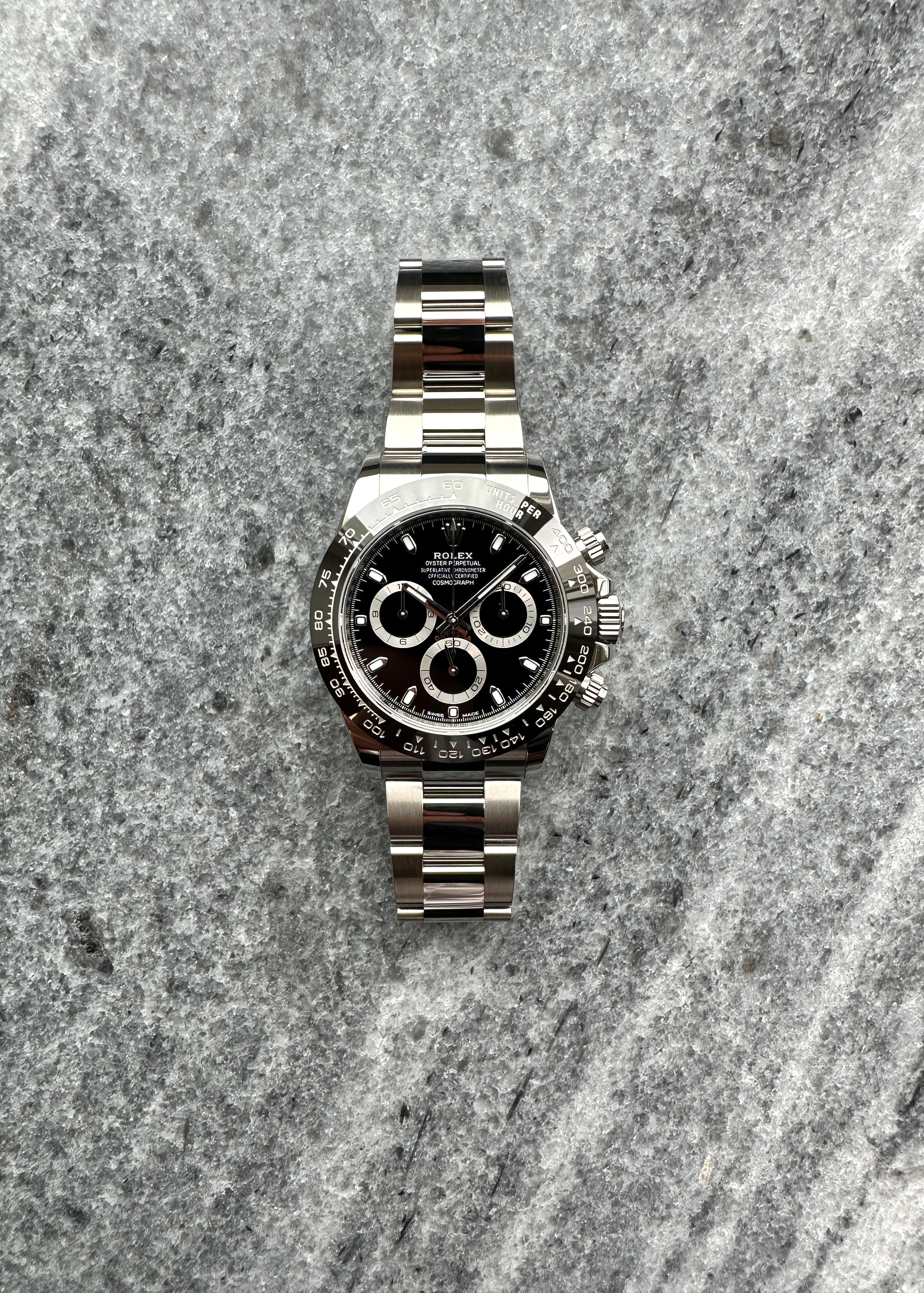 Eine Rolex Daytona 116500LN aus Stahl mit schwarzem Zifferblatt liegt auf einem grauen Steinhintergrund