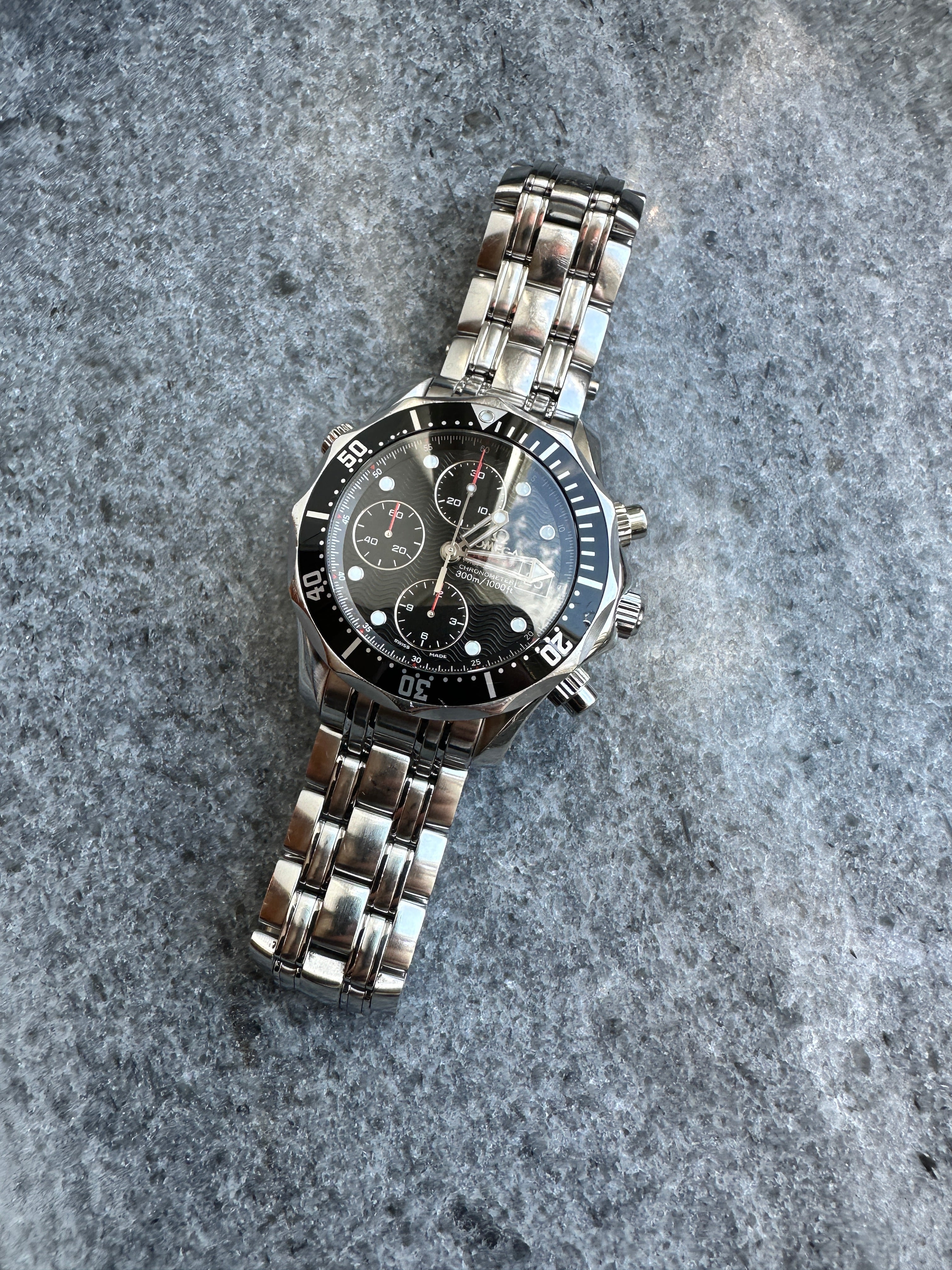 Omega Seamaster Diver Chronograph (2013) Automatik-Uhr aus Edelstahl auf grauem Stein mit Blick von oben