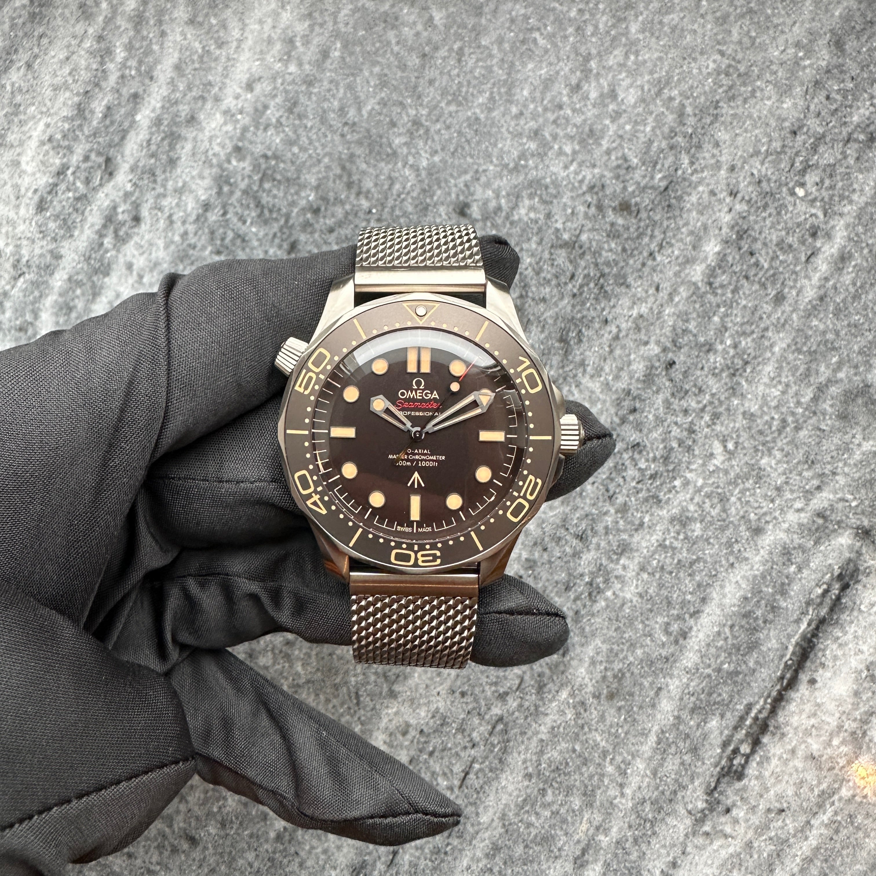 Omega Seamaster Diver 300m "James Bond" 007 aus Titan mit Mesh-Armband auf grauem Stein mit gloved hand