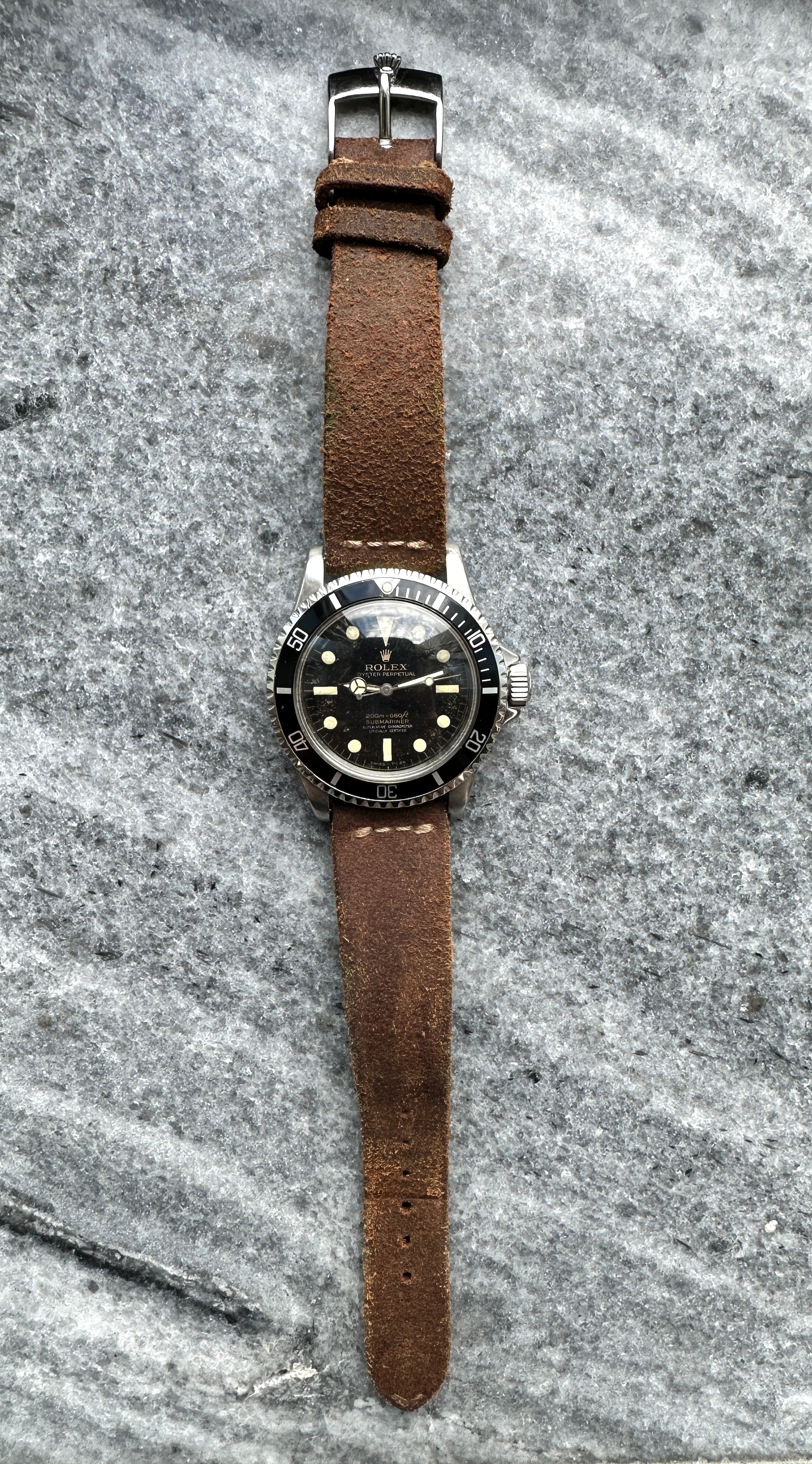 Rolex Submariner 5512 von 1963 mit braunem Lederarmband auf grauem Stein