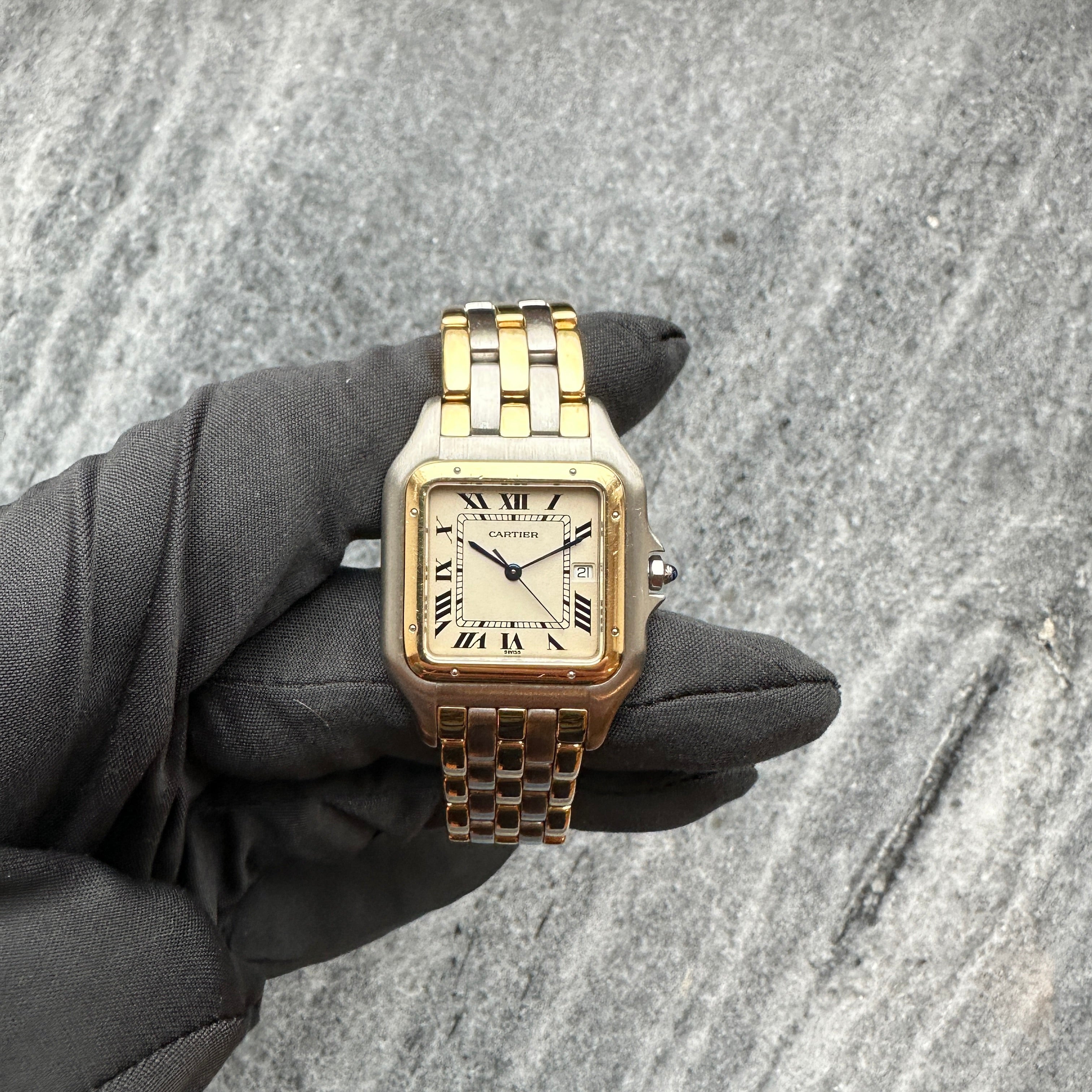 Eine Cartier Panthere Jumbo Vintage 1986 Uhr mit zweifarbigem Stahlarmband und rechteckigem Zifferblatt auf graublauem Hin…