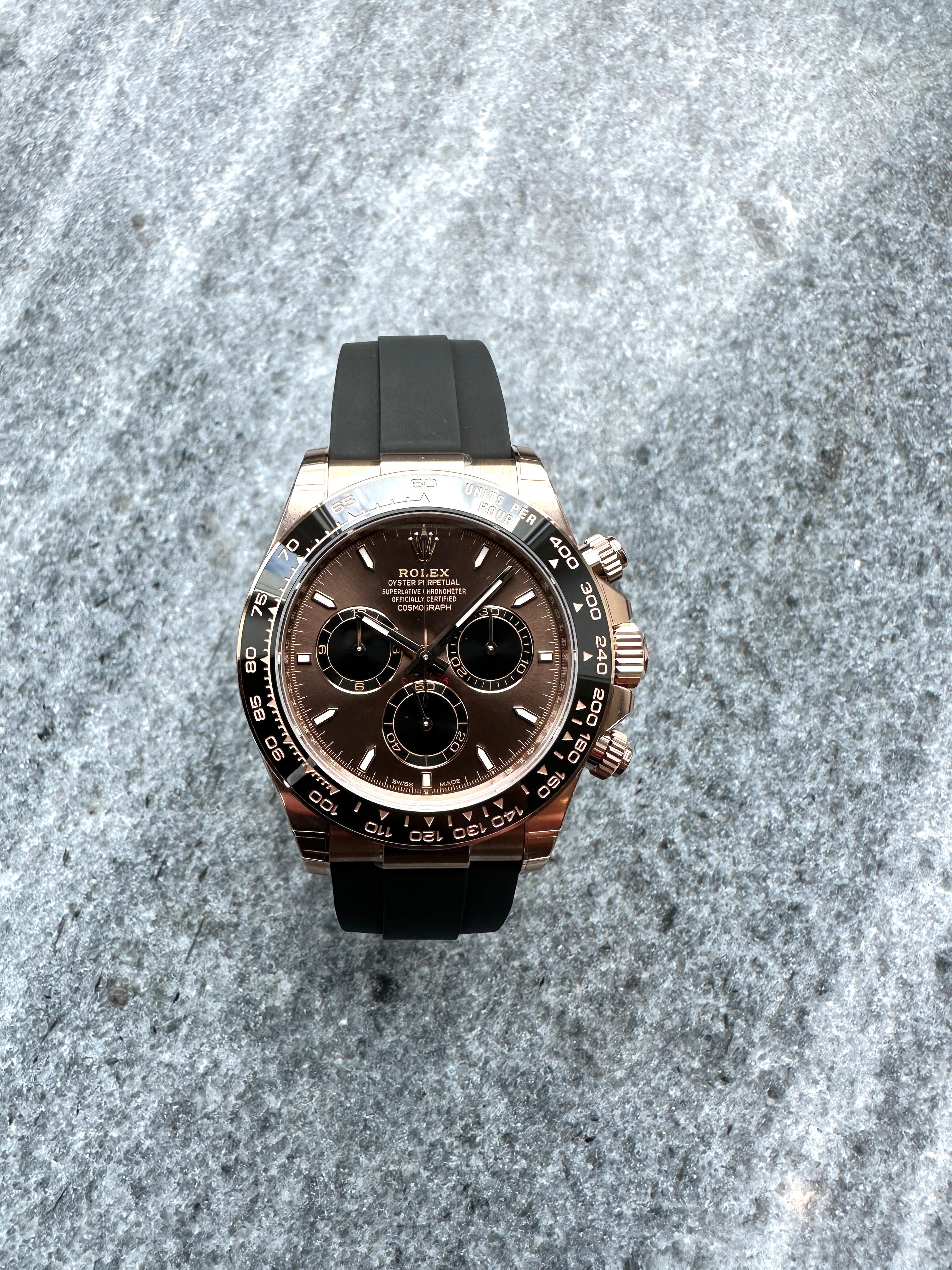 Rolex Cosmograph Daytona in Roségold mit braunem Zifferblatt und Kautschukband auf grauem Stein