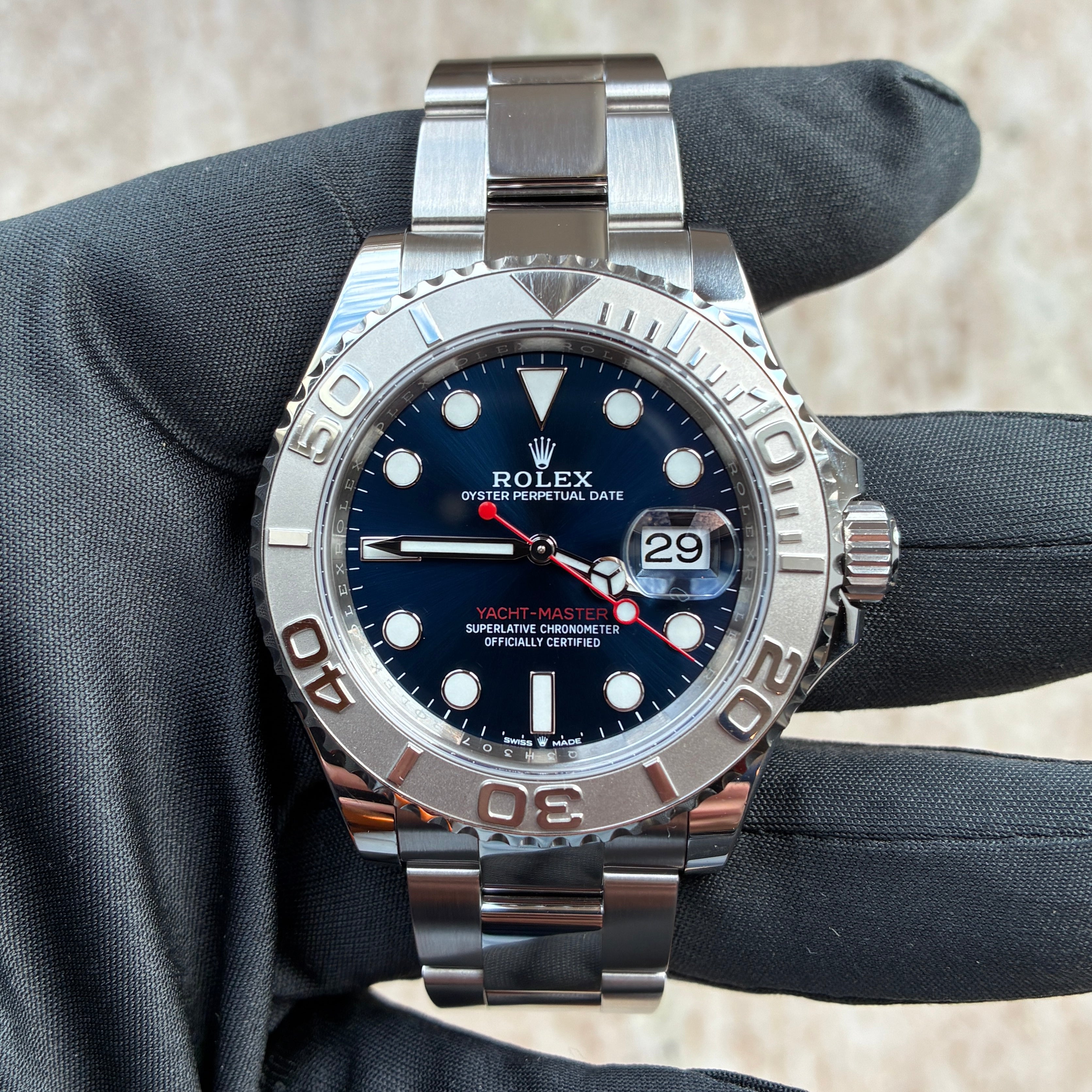 Eine Rolex Yacht-Master 40 mit blauem Zifferblatt und Edelstahlgehäuse wird von einer schwarzen Handschuhhand gehalten