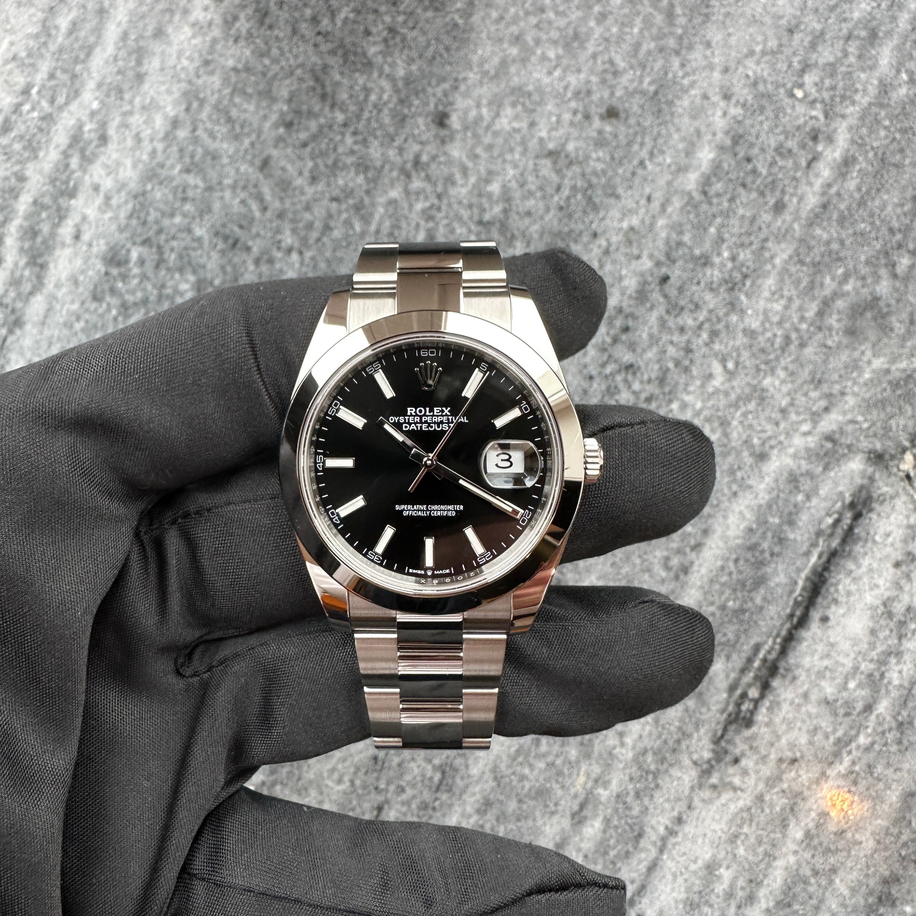 Rolex Datejust 41 mit schwarzem Zifferblatt in Frontansicht, gehalten in einer schwarzen Handschuh-Aufnahme