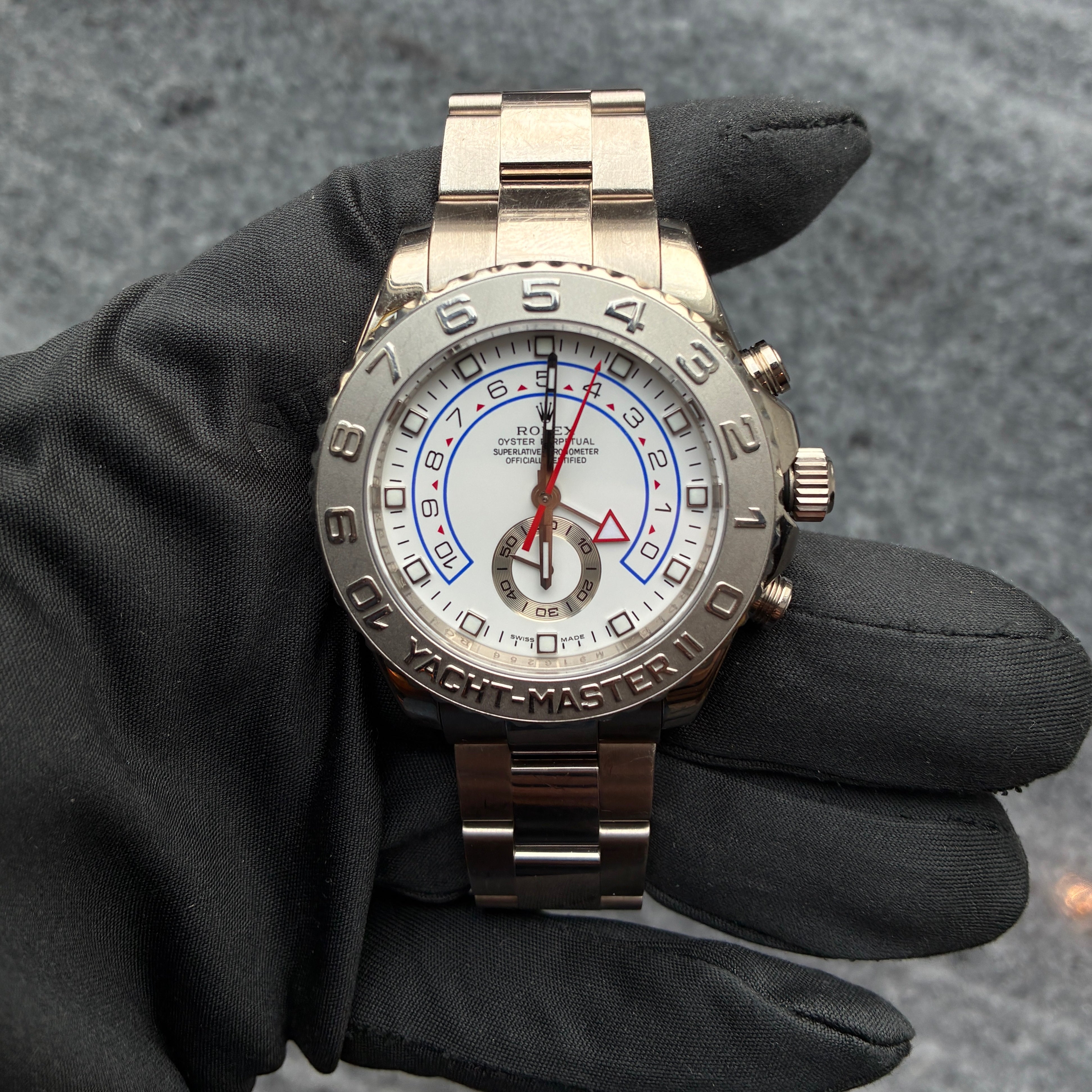 Rolex Yacht-Master II aus Weissgold mit weissem Zifferblatt und rotem Dreieck-Marker, gehalten von einer Hand in schwarzer Handschuh