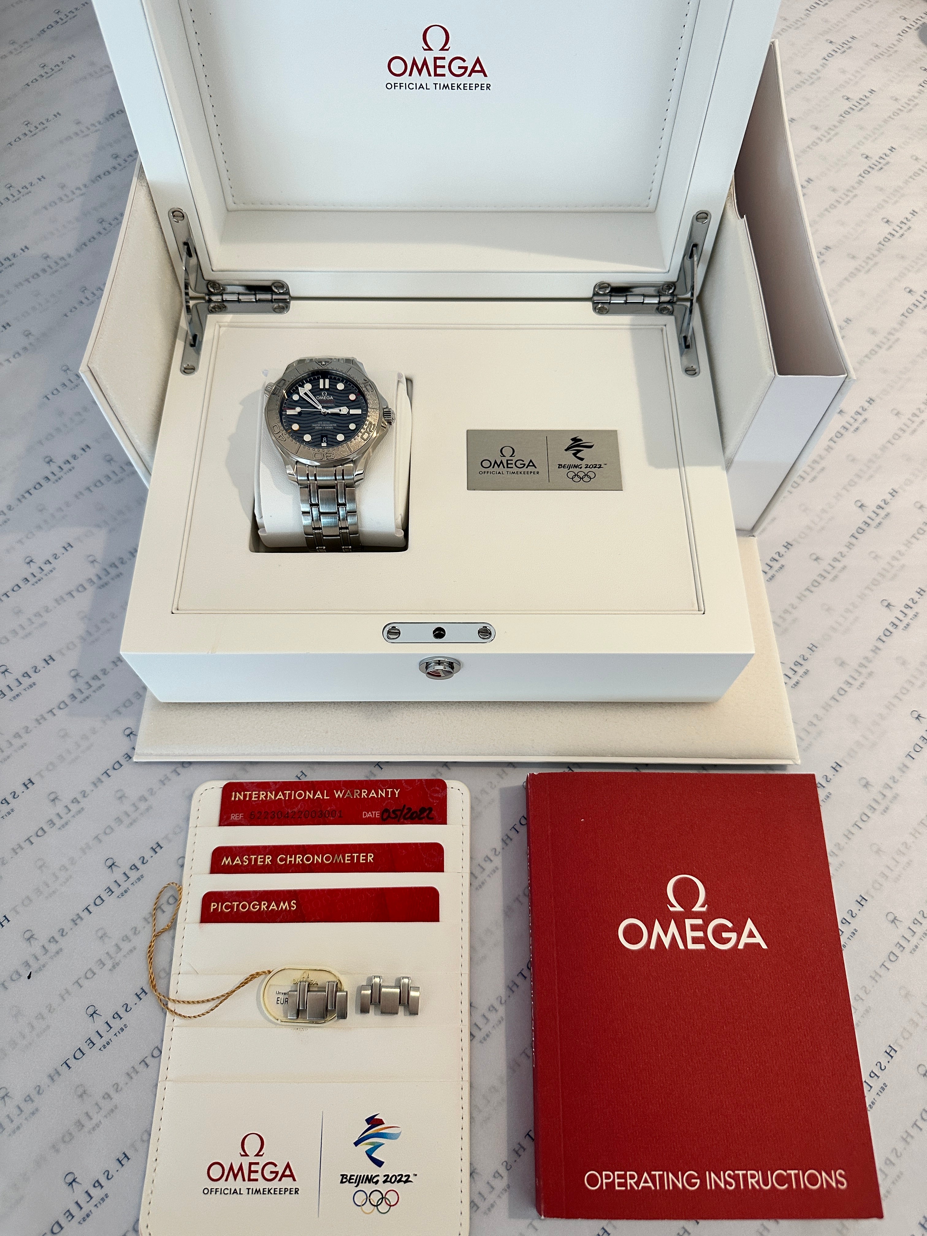Omega Seamaster Diver 300M Beijing 2022, neuwertig, im geöffneten Umkarton auf weißem Untergrund mit Zubehör