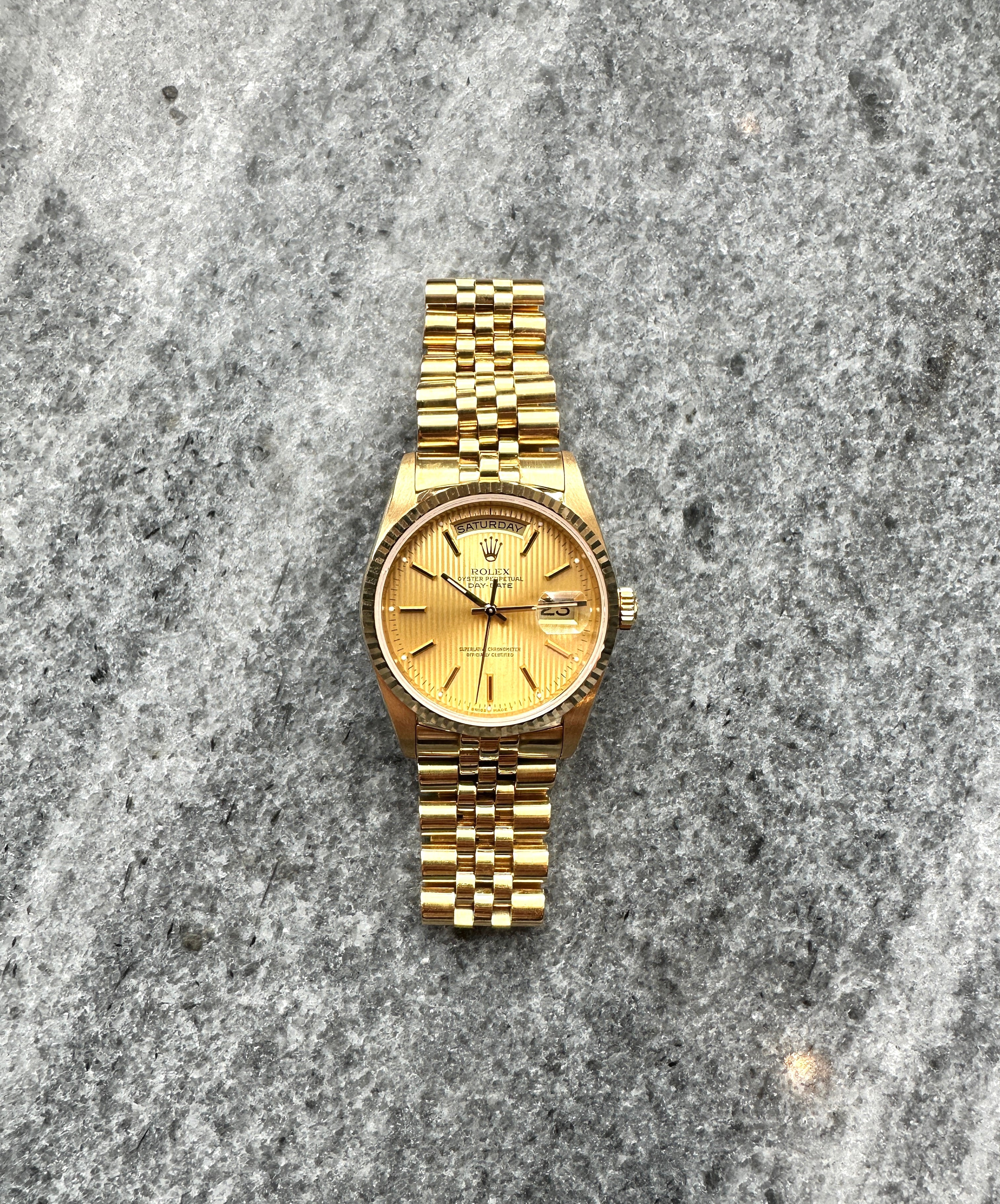 Rolex Day-Date 36 Tapestry Dial aus Gelbgold mit geriffeltem Zifferblatt und 10 Indexen auf steinigem Hintergrund