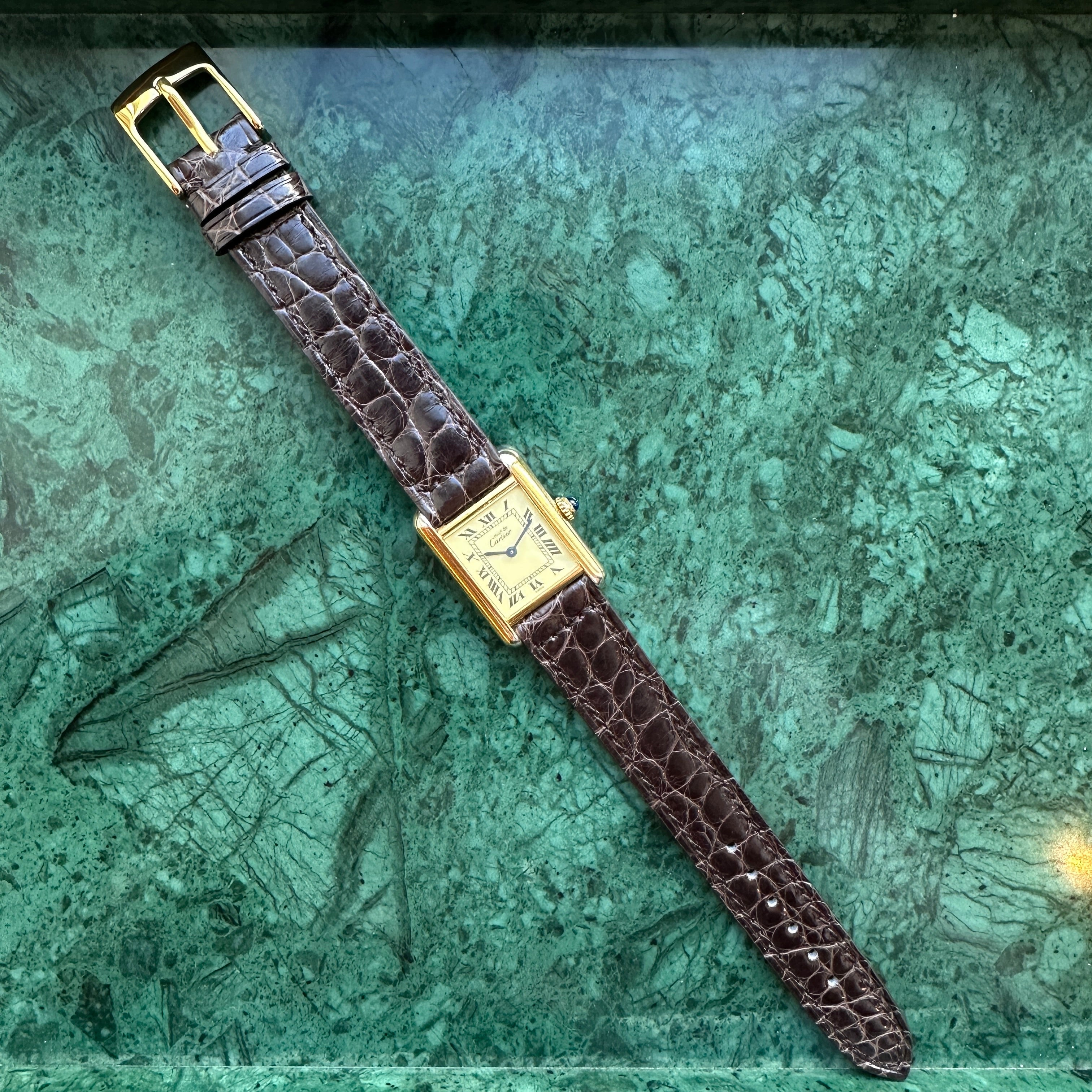 Cartier Tank Vermeil Ref. 5057001 mit dunkelbraunem Kroko-Lederarmband auf gruenem Marmorhintergrund
