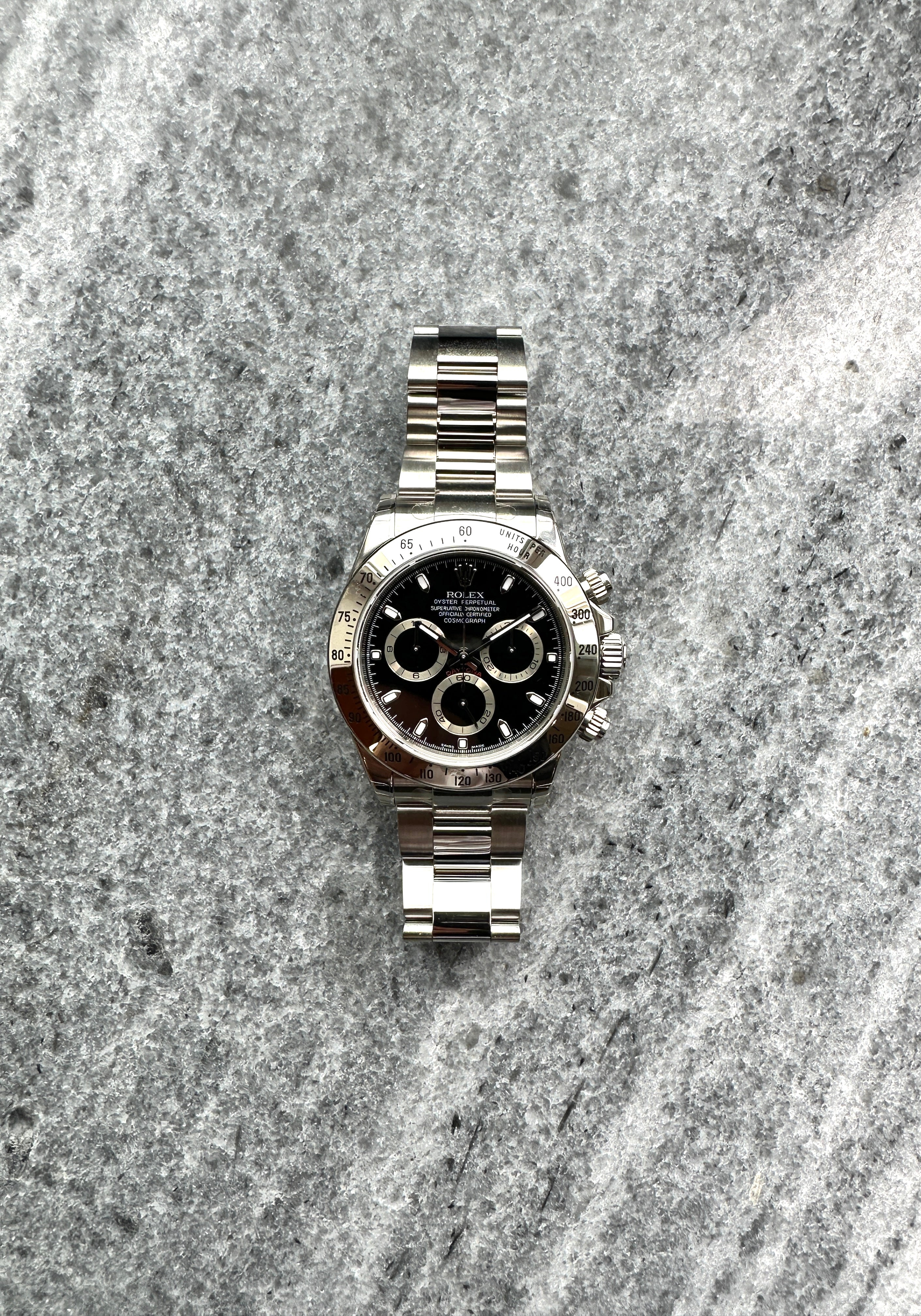 Rolex Daytona 116520 mit schwarzem Zifferblatt auf grauem Steinuntergrund, Edelstahlarmband