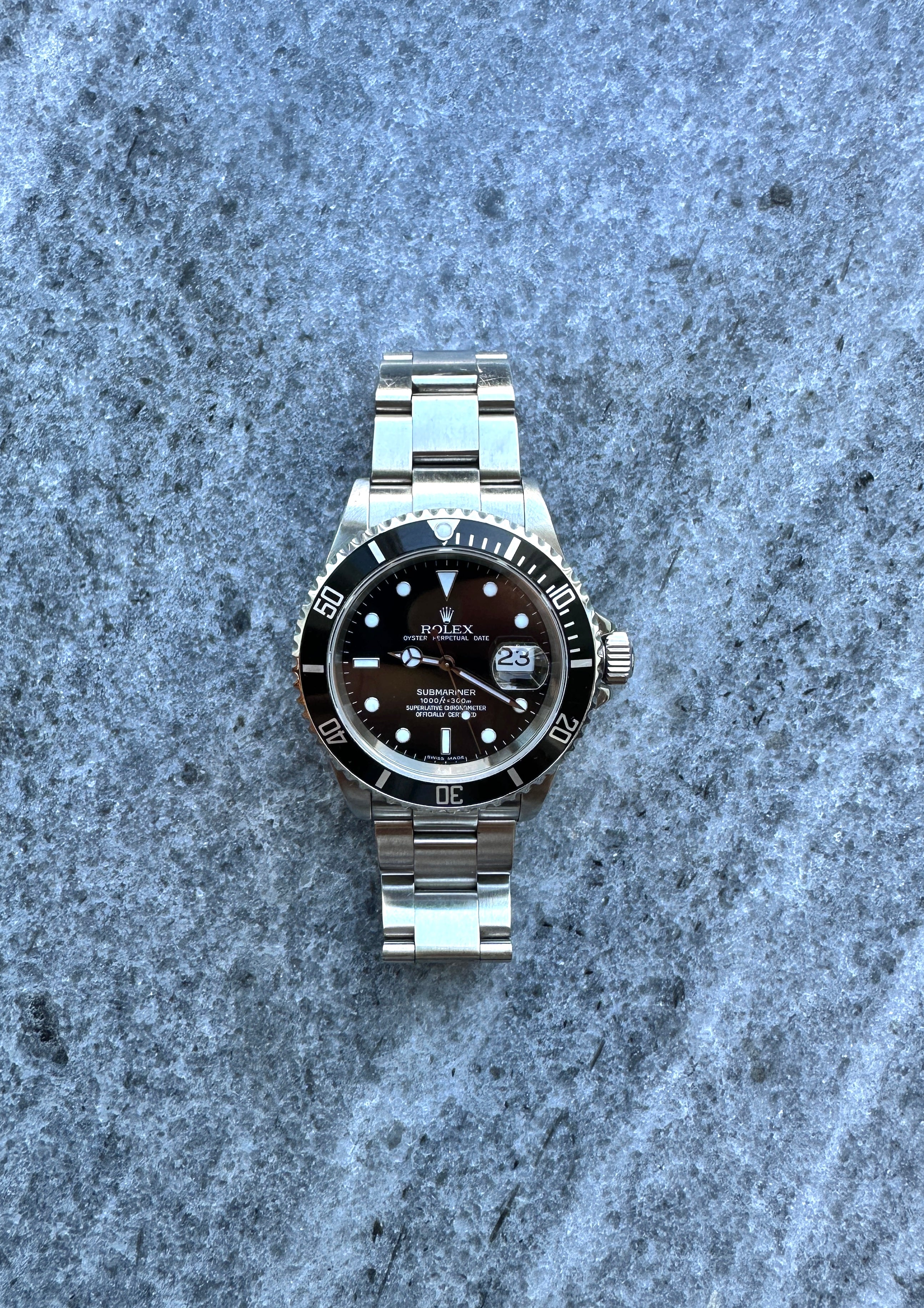 Rolex Submariner Date 16610 aus Edelstahl mit schwarzem Zifferblatt und Datumskomplikation auf strukturiertem Untergrund