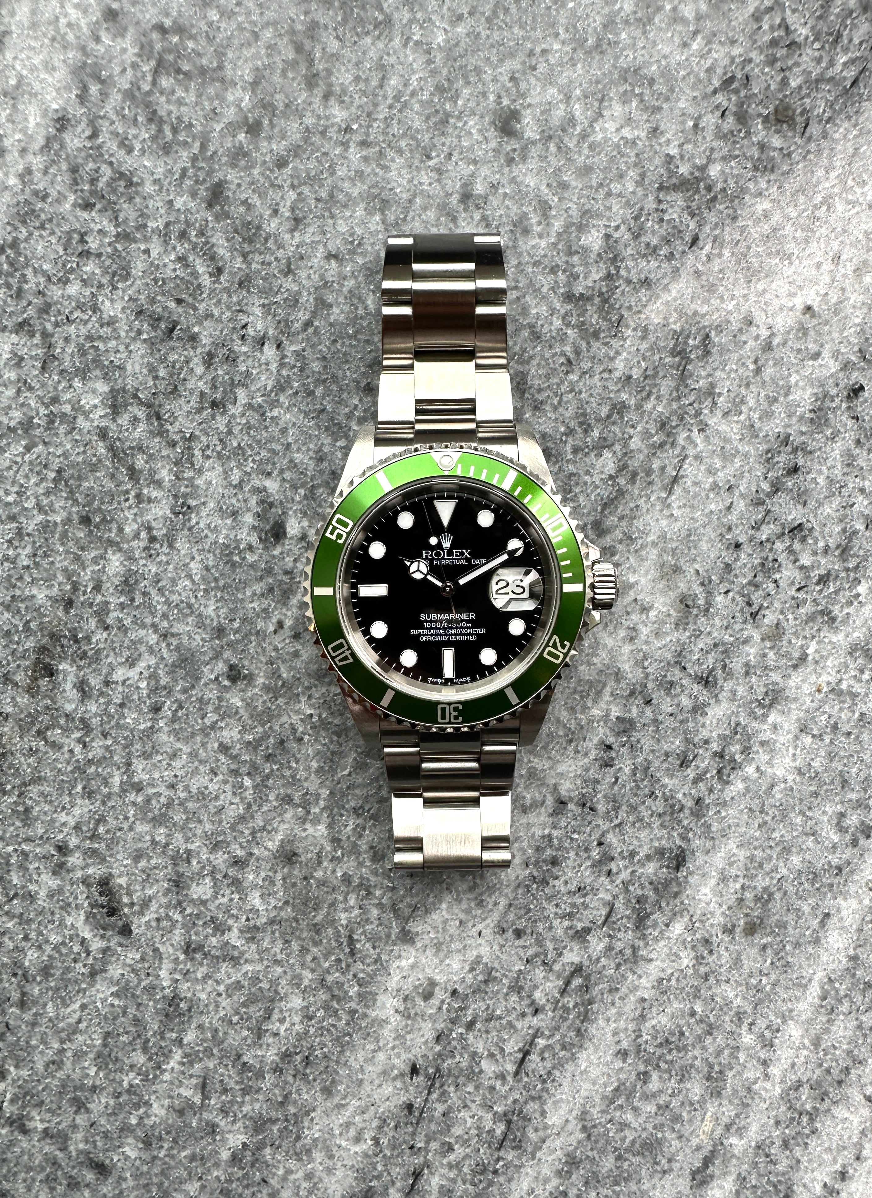 Rolex Submariner Date "Kermit" von 2004, Frontansicht auf grauem Untergrund mit 11 Indexen und 3 Zeigern