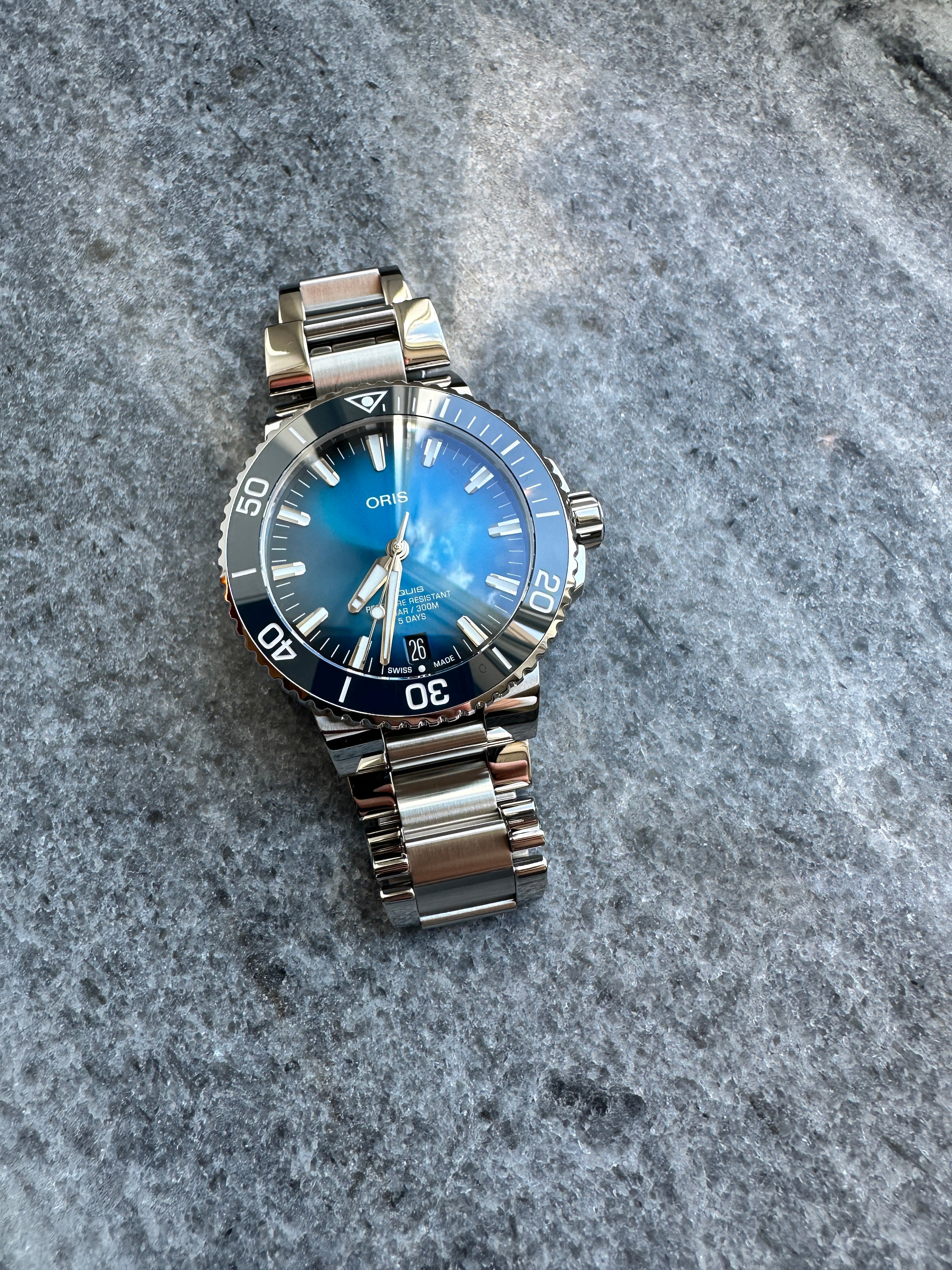 Oris Aquis Date Calibre 400 Automatik mit blauem Zifferblatt und Edelstahlarmband auf grauem Steinuntergrund