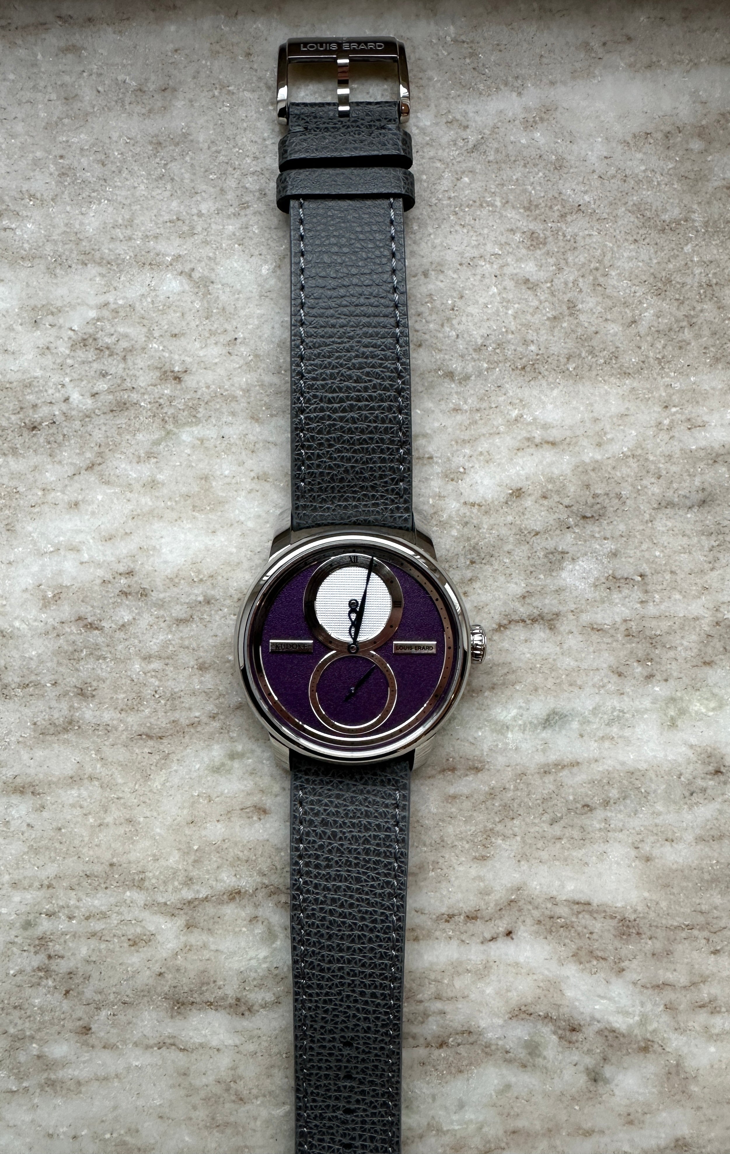 Louis Erard Le Régulateur x Kudoke Purple mit grauem Lederarmband und Edelstahlgehäuse auf Marmor