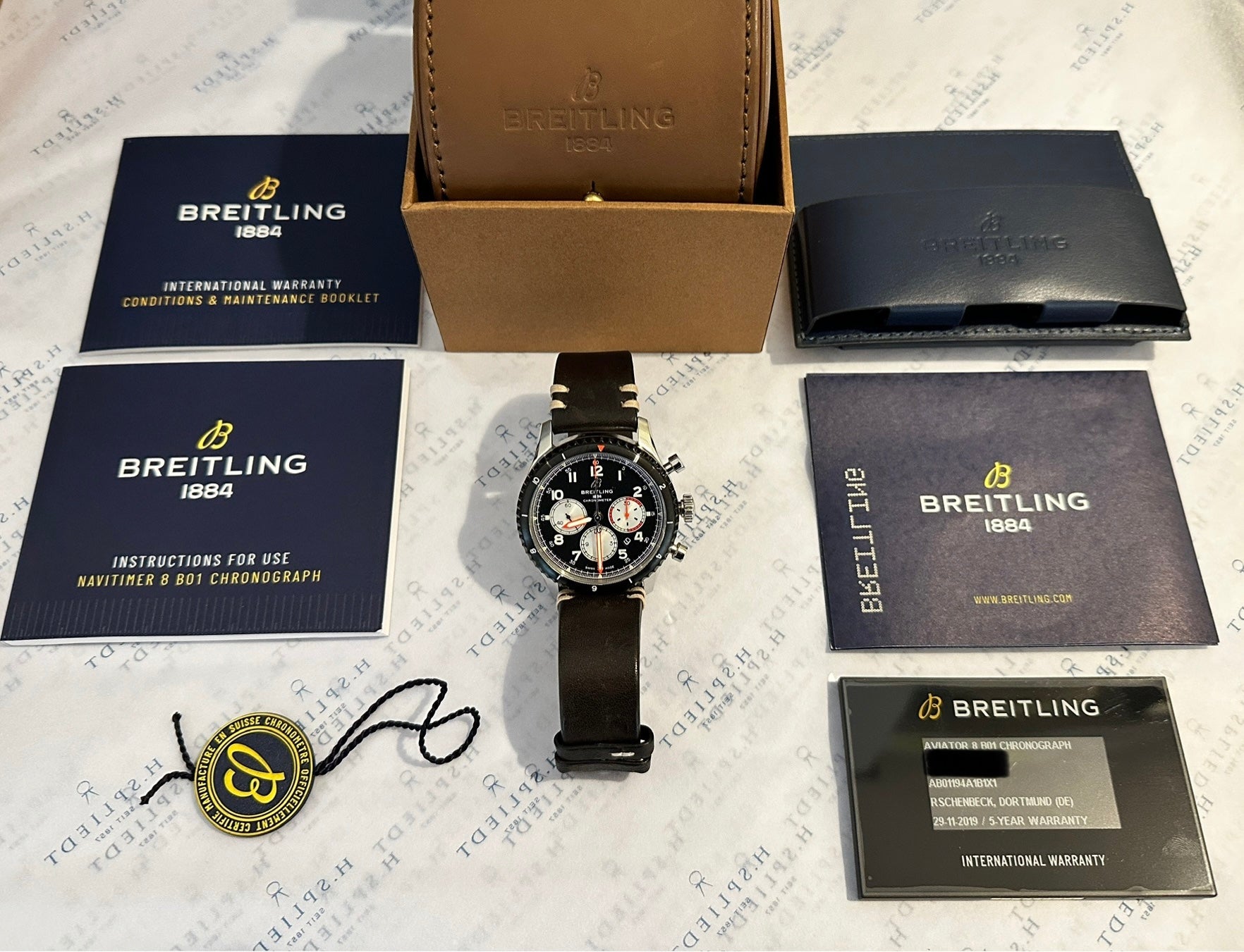 Breitling Aviator 8 B01 Chronograph 43 Mosquito mit braunem Lederband und Zubehör auf strukturiertem Papier