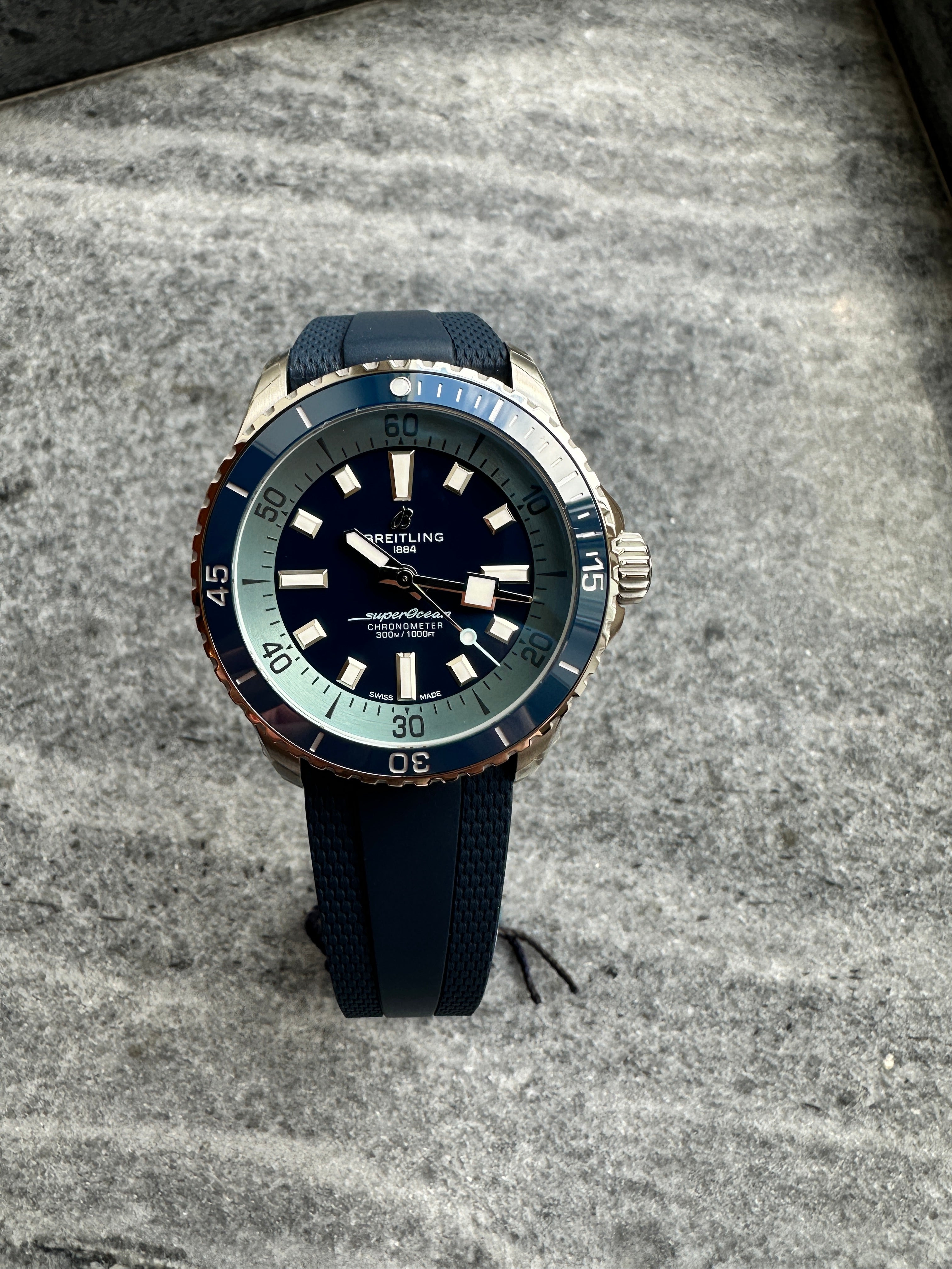Breitling Superocean Automatic 42 Sylt Edition, Frontansicht, blaue Lünette und Zifferblatt auf grauem Stein