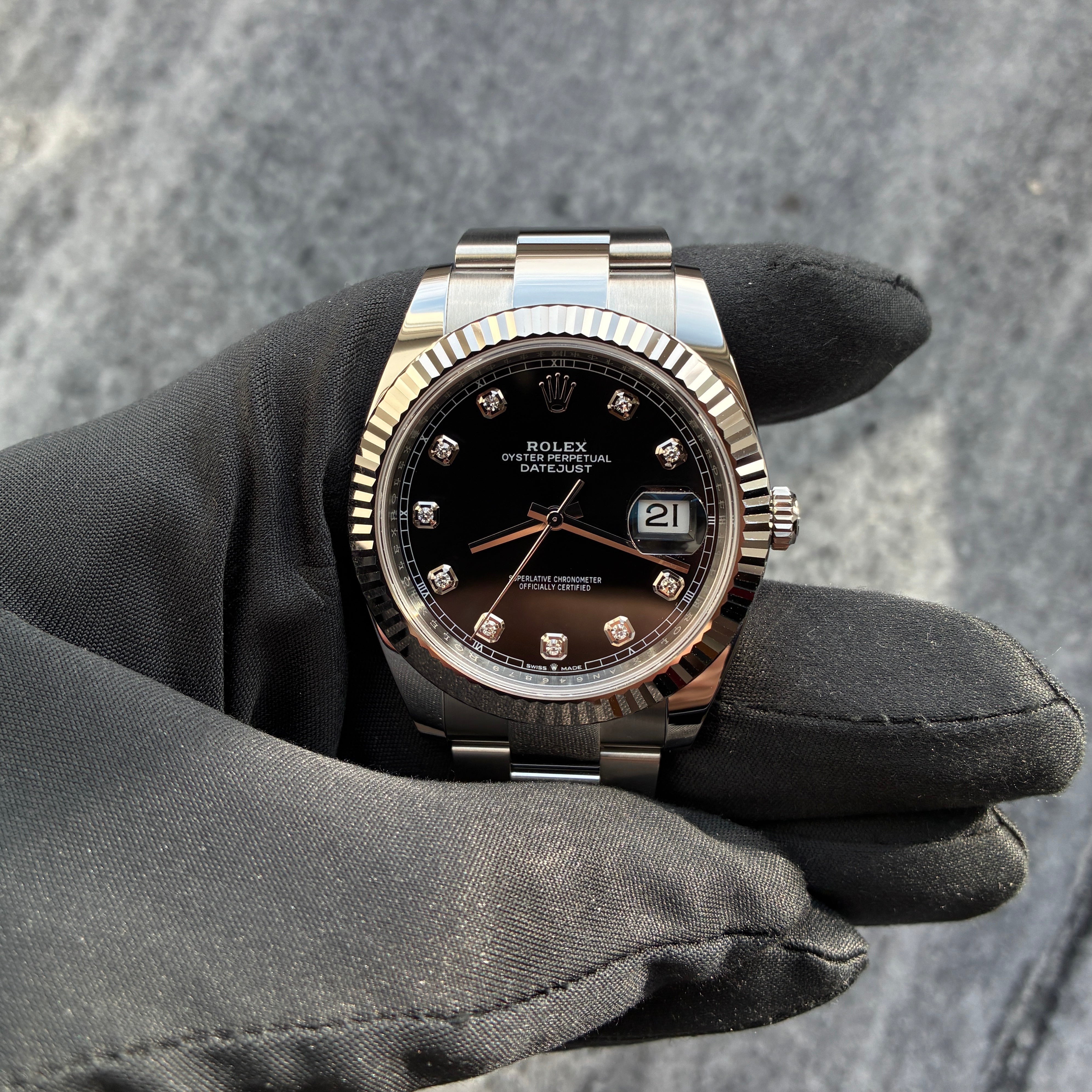 Rolex Datejust 41 Automatik mit schwarzem Zifferblatt und Diamanten auf grauem Stoffhintergrund