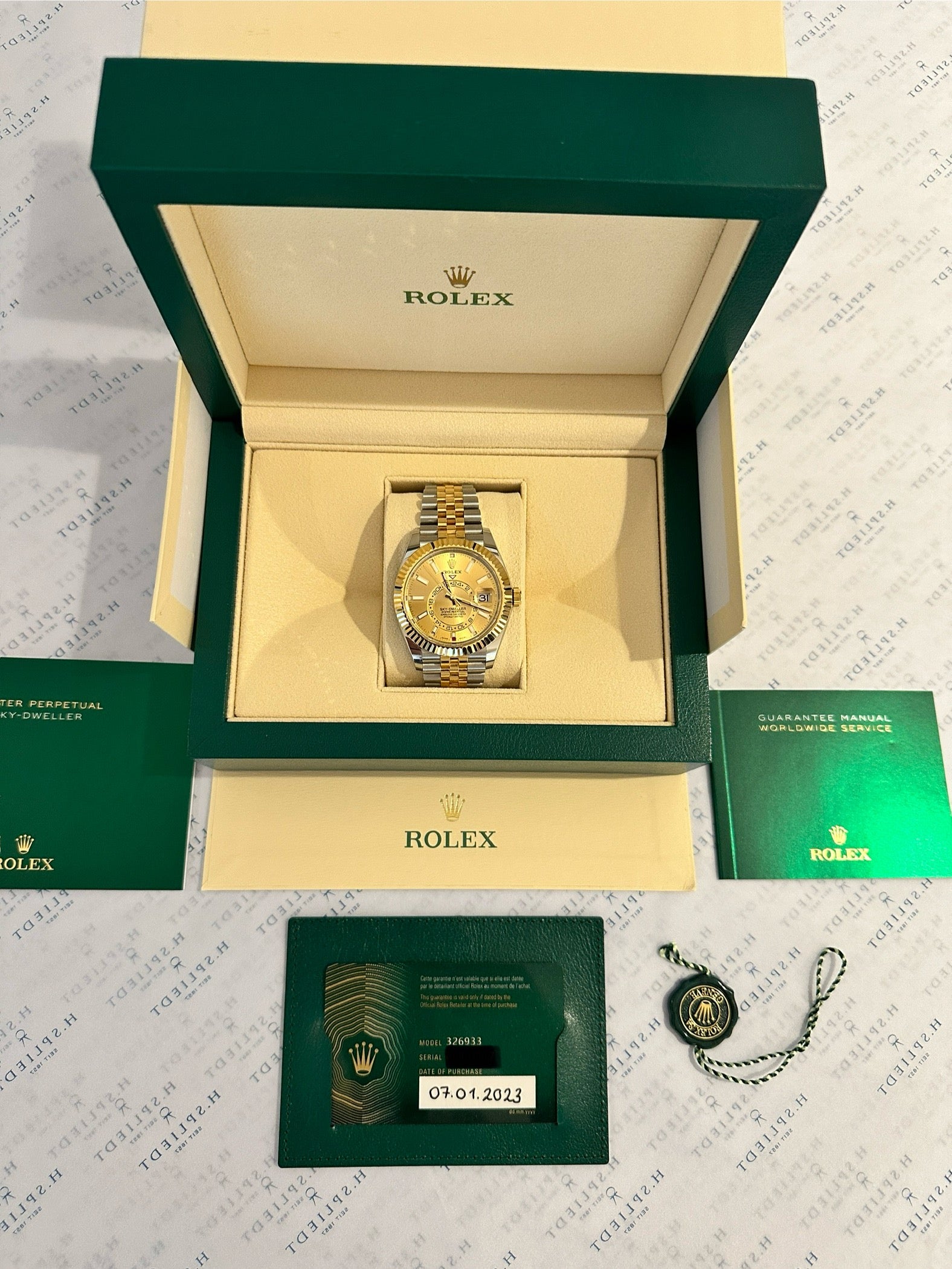 Rolex Sky-Dweller Stahl-Gold Jubilee im geöffneten grünen Karton auf weißem Untergrund mit Papieren