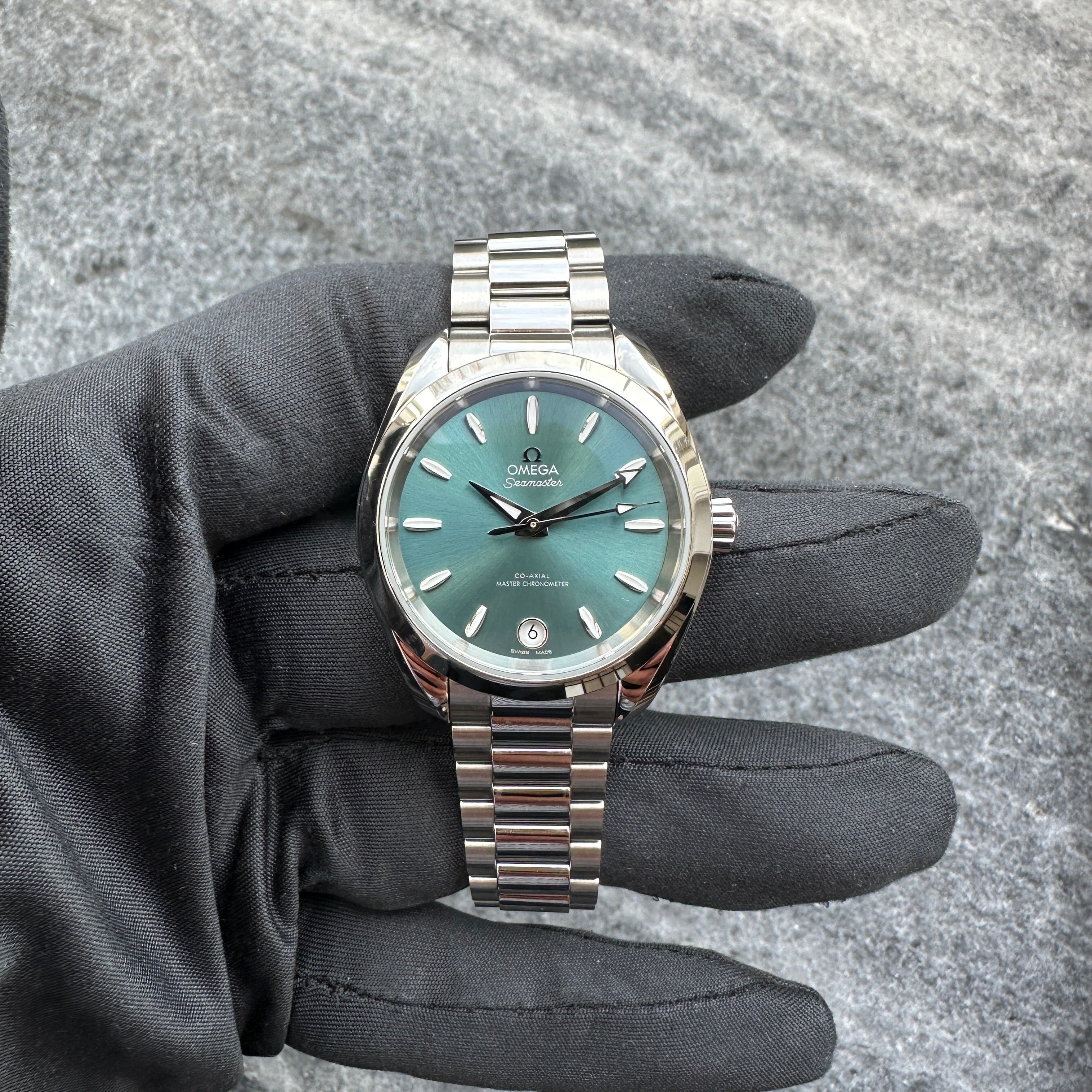 Omega Seamaster Aqua Terra 34mm Petrol mit Stahlarmband im Detail, präsentiert auf schwarzem Stoff