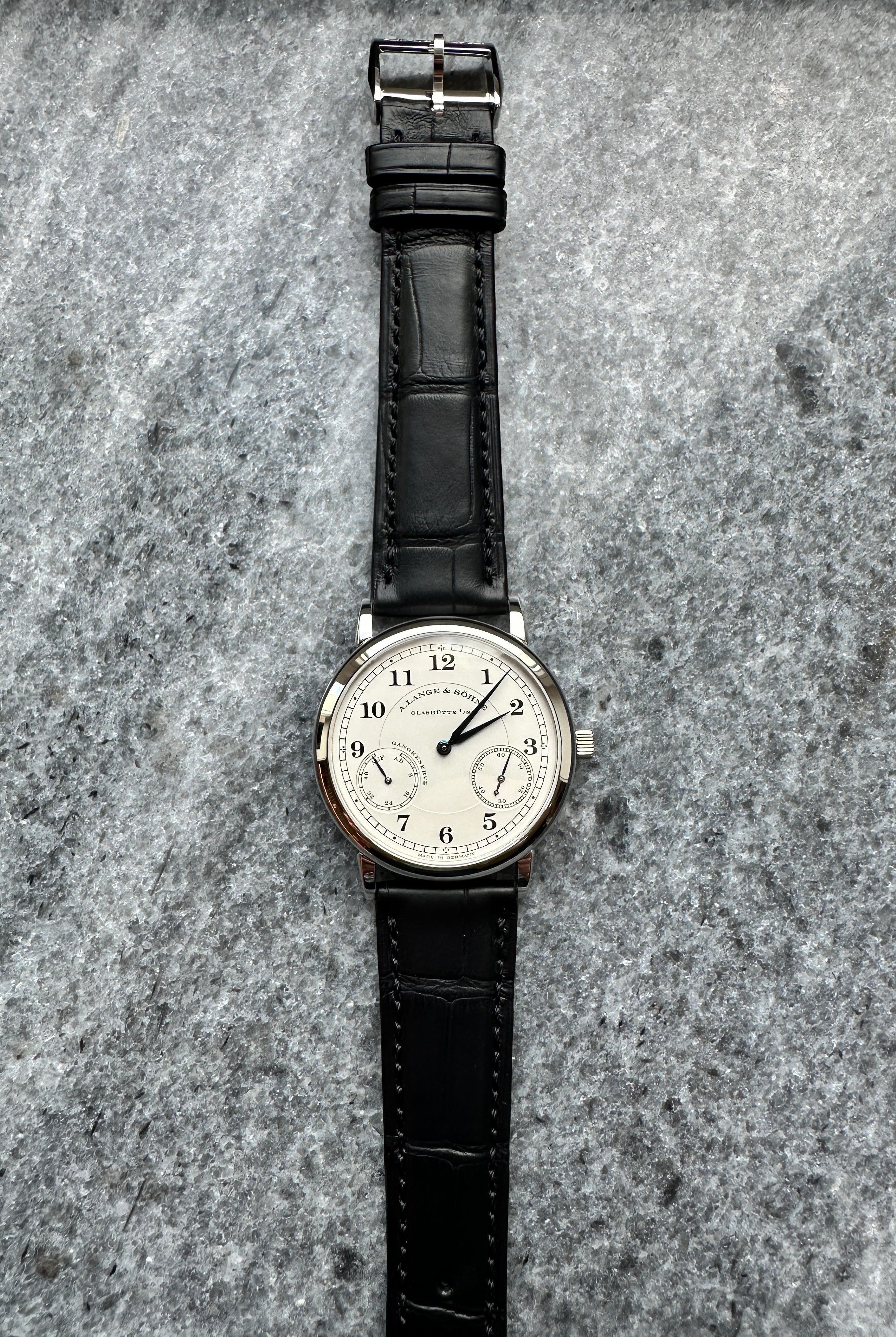 A. Lange & Söhne 1815 Up Down aus Platin mit schwarzem Lederarmband auf Steinuntergrund