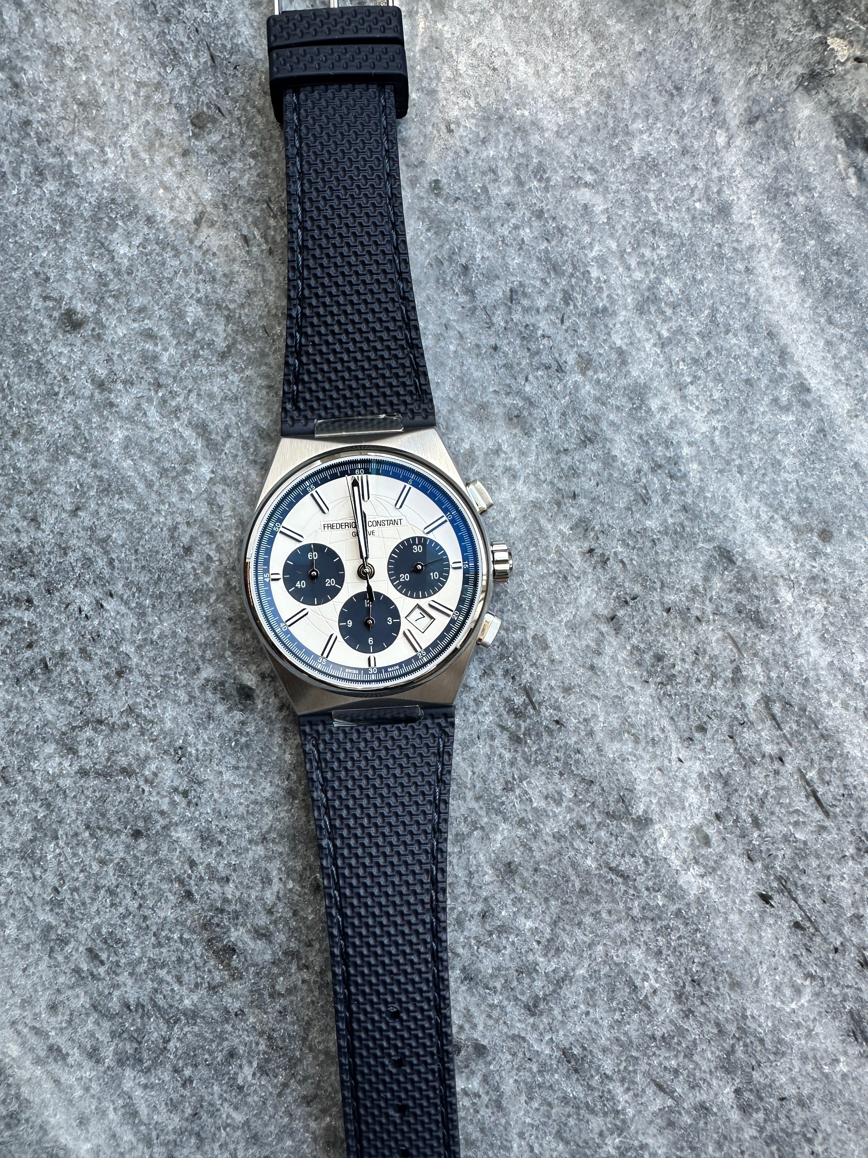 Frederique Constant Highlife Chronograph aus Edelstahl mit weißem Zifferblatt und blauem Band auf grauem Stein