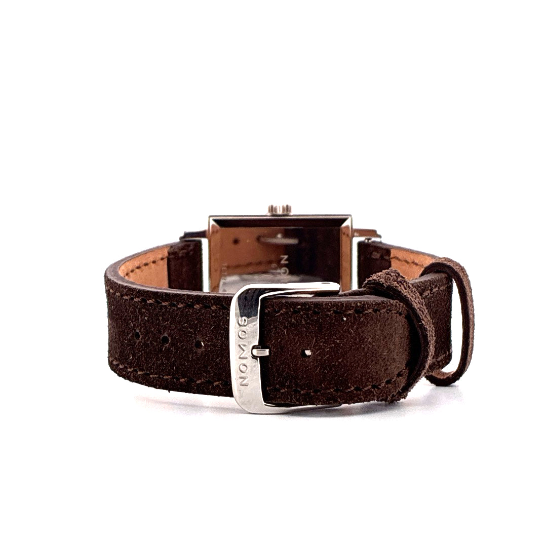 Nahaufnahme der Nomos Tetra 27 Karat mit braunem Suede-Armband und Dornschließe