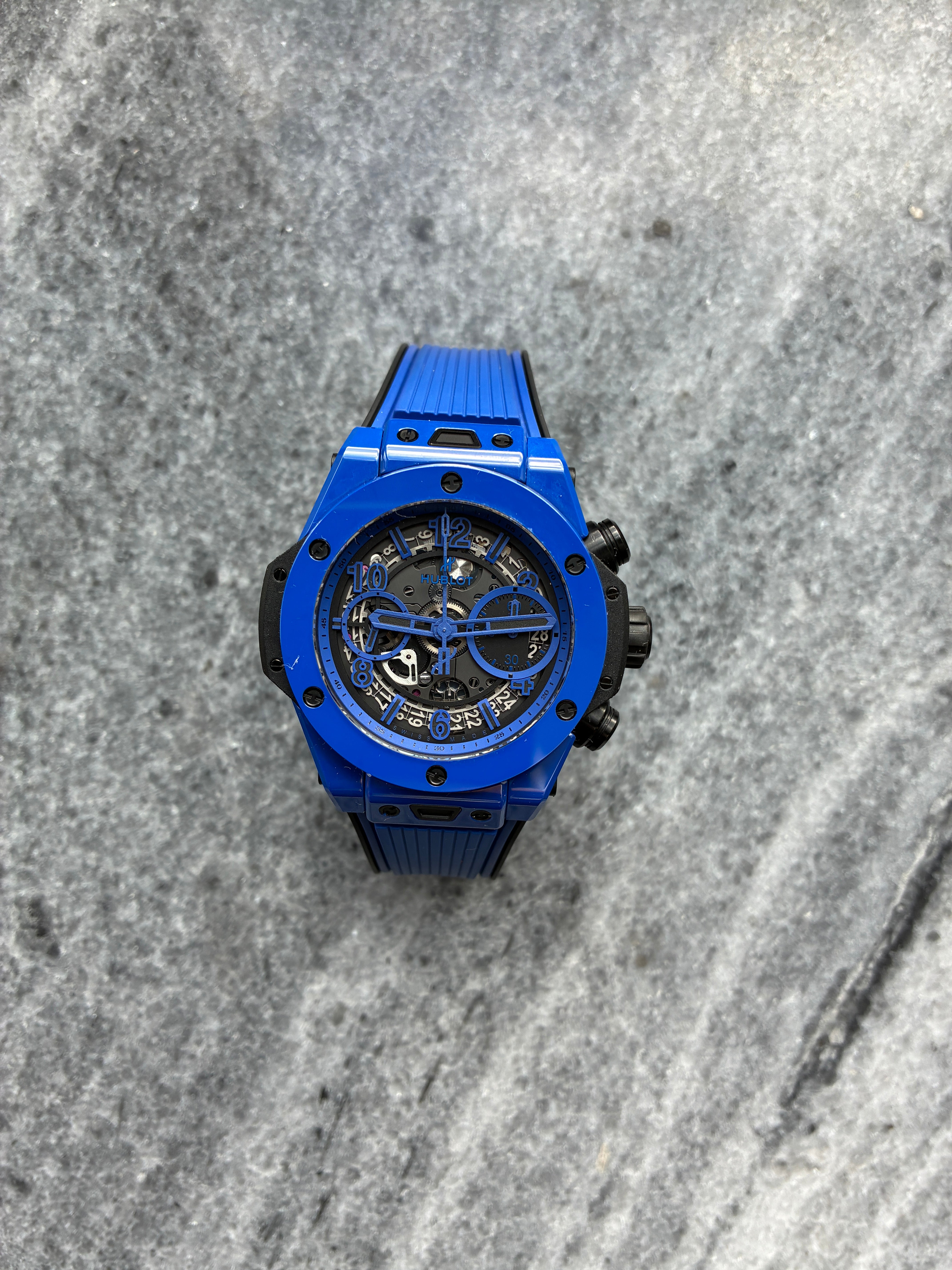 Eine blaue Hublot Big Bang Unico Skeleton mit schwarzem Kautschukarmband auf grauem Steinboden
