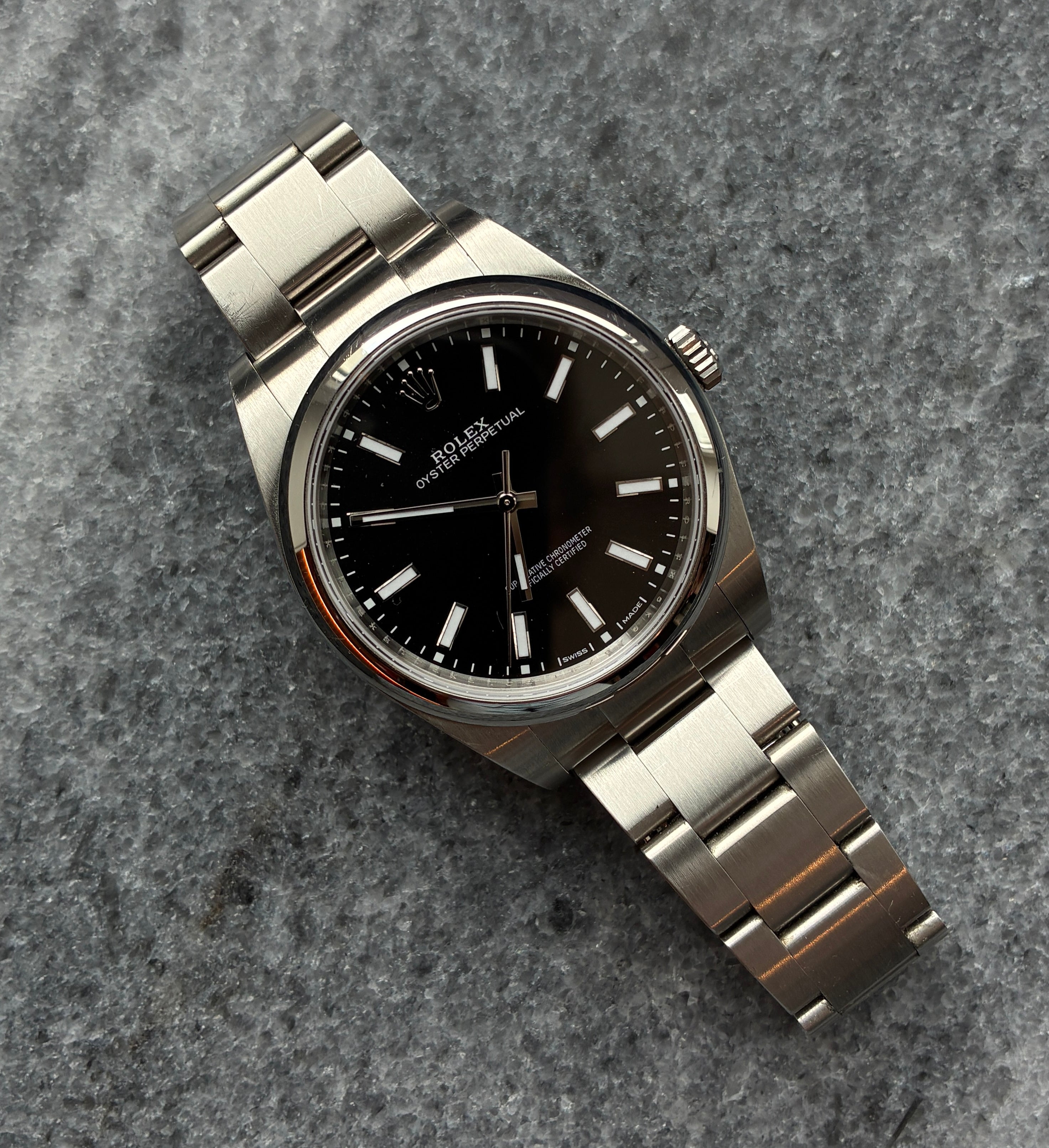 Rolex Oyster Perpetual 39 mit schwarzem Zifferblatt und Stahlarmband auf grauem Steinuntergrund