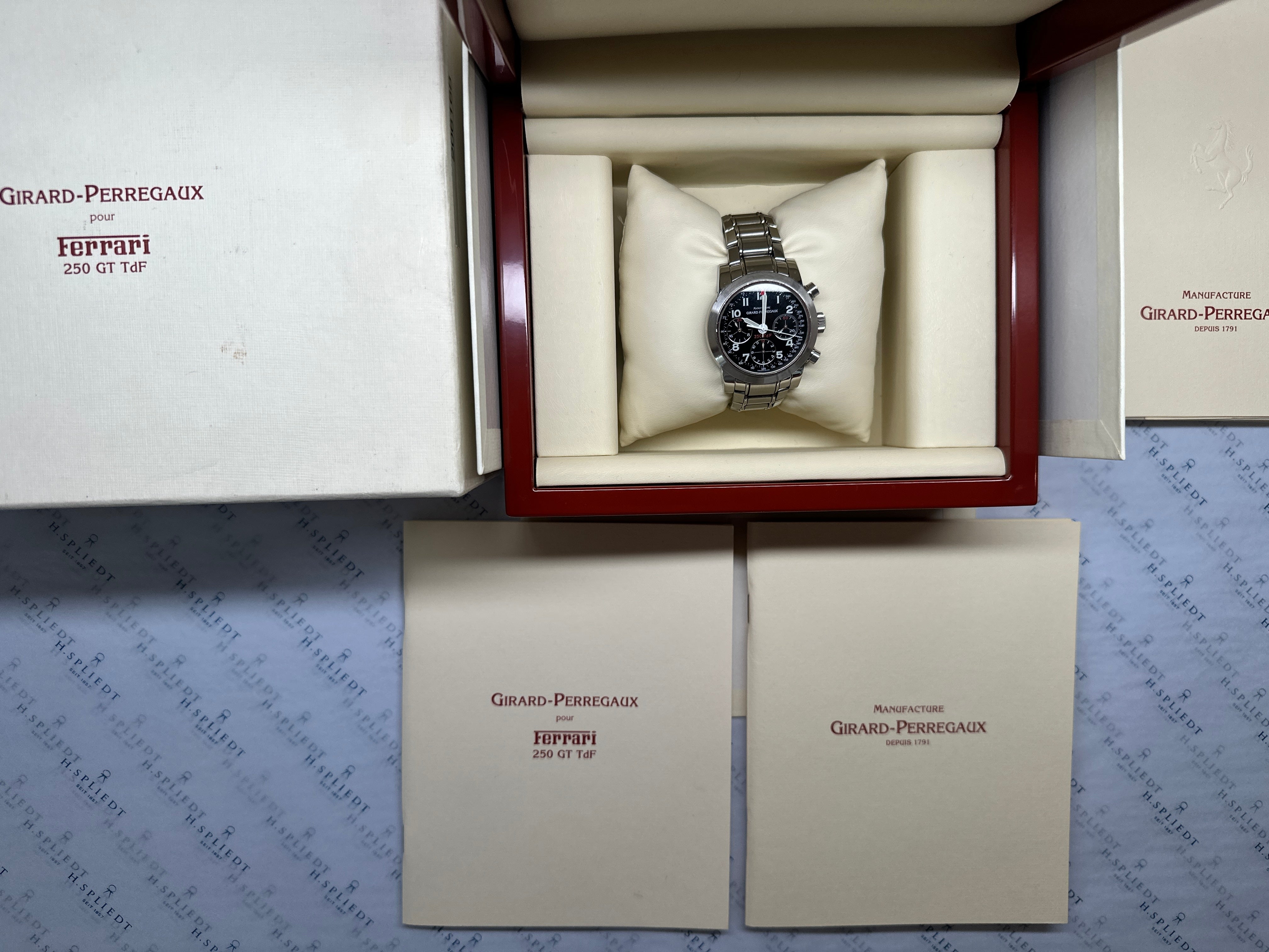 Girard Perregaux Ferrari 250 GT TdF Chronograph Edelstahl auf hellem Kissen im roten Uhrenkasten