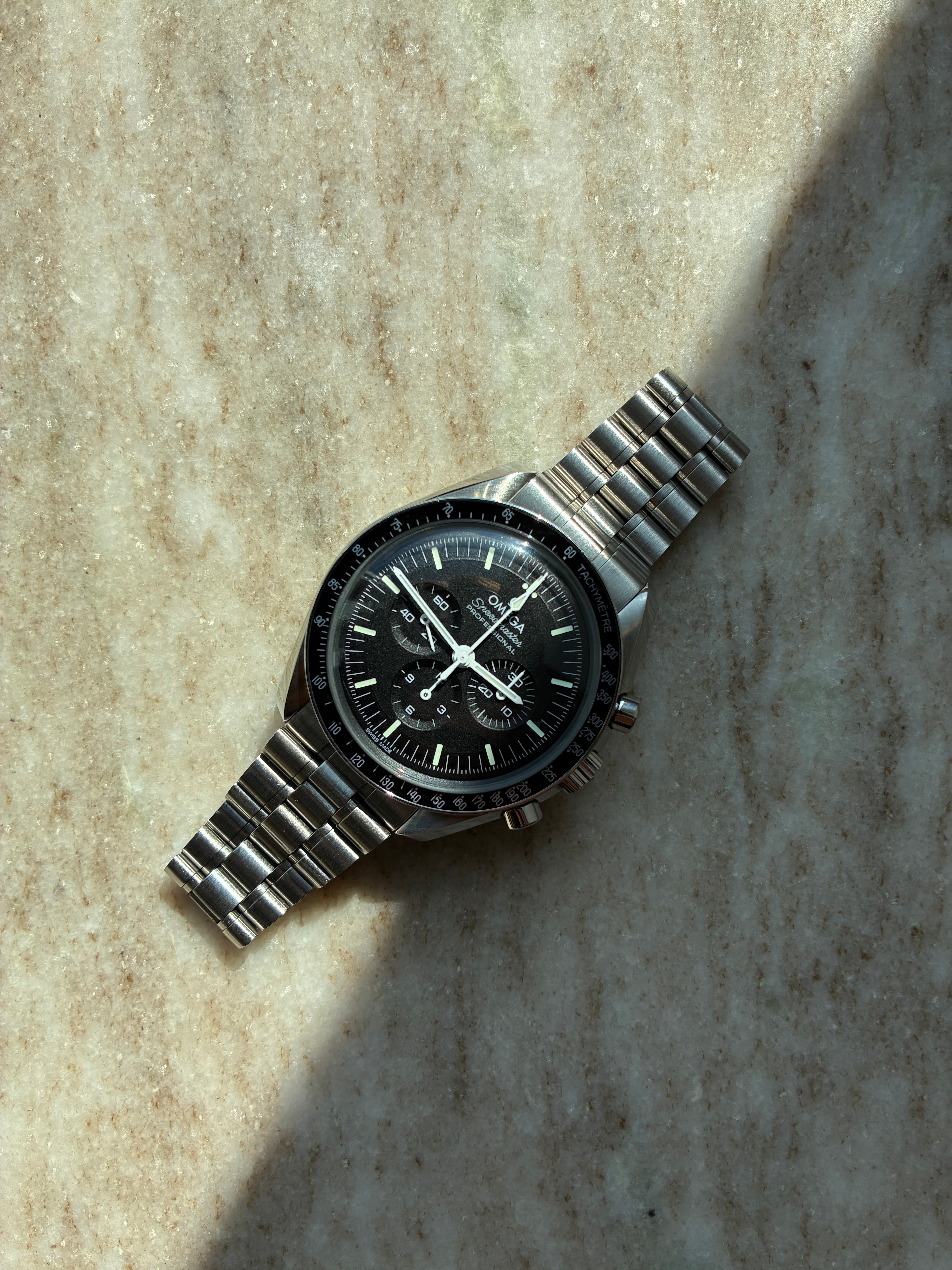 Omega Speedmaster Professional Moonwatch mit schwarzem Zifferblatt und Edelstahlarmband auf Marmor