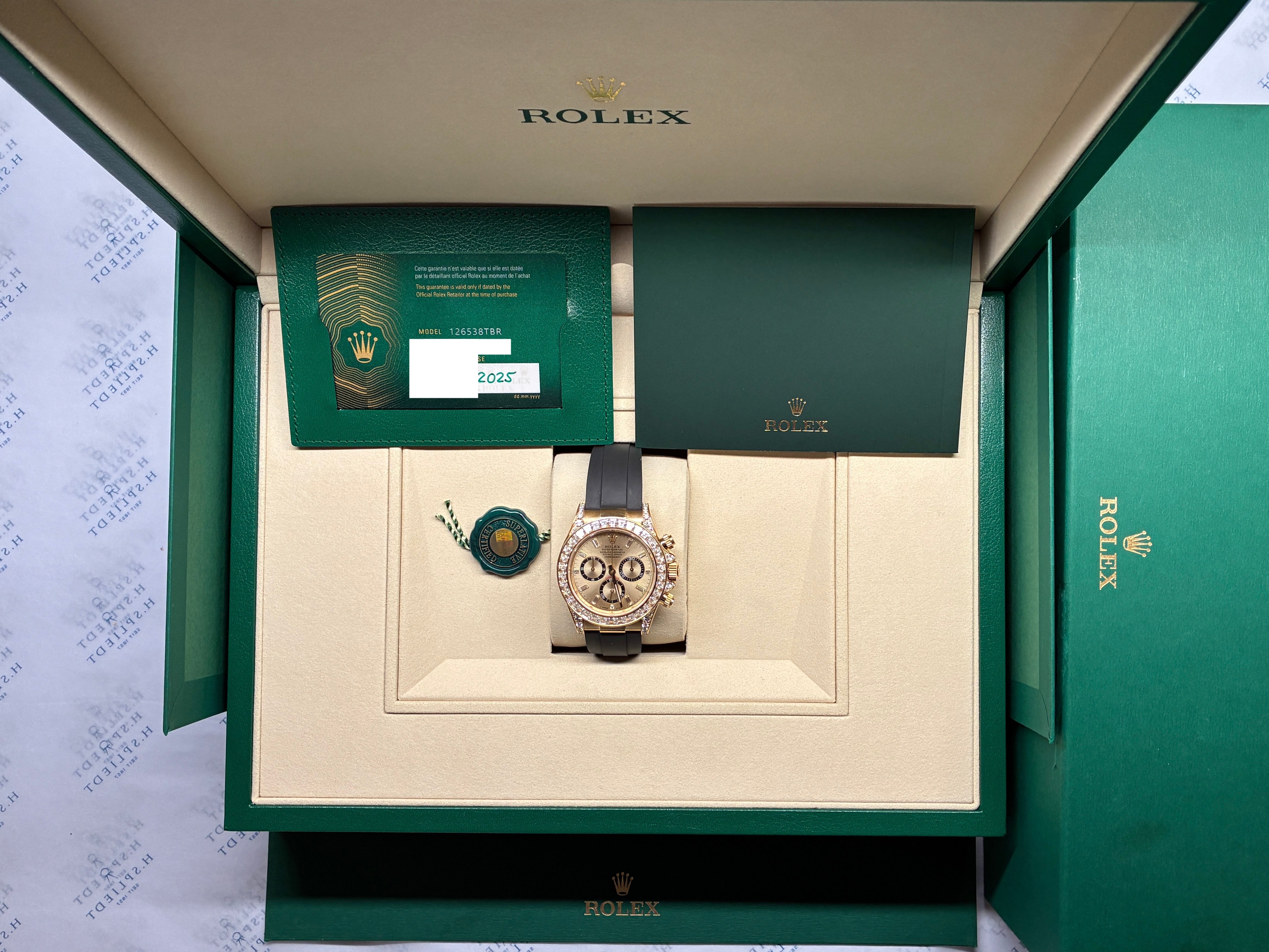 Eine Rolex Cosmograph Daytona mit Diamantlünette liegt in geöffneter grüner Verpackung auf einem hellen Innenteil neben Garantiekarten