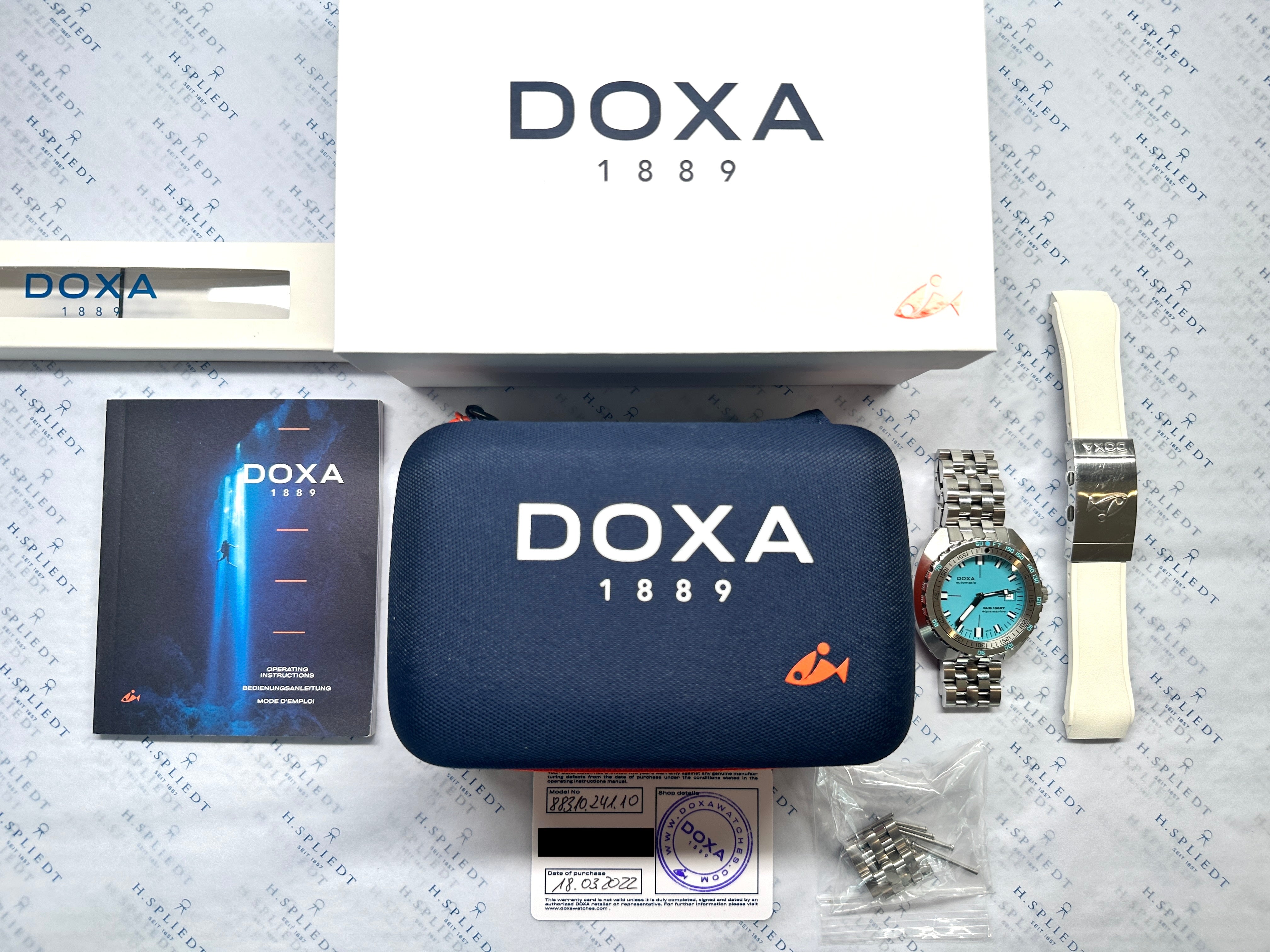 DOXA Sub 1500t Herrenuhr Aquamarin mit Stahlarmband und Zubehör auf gemustertem Hintergrund