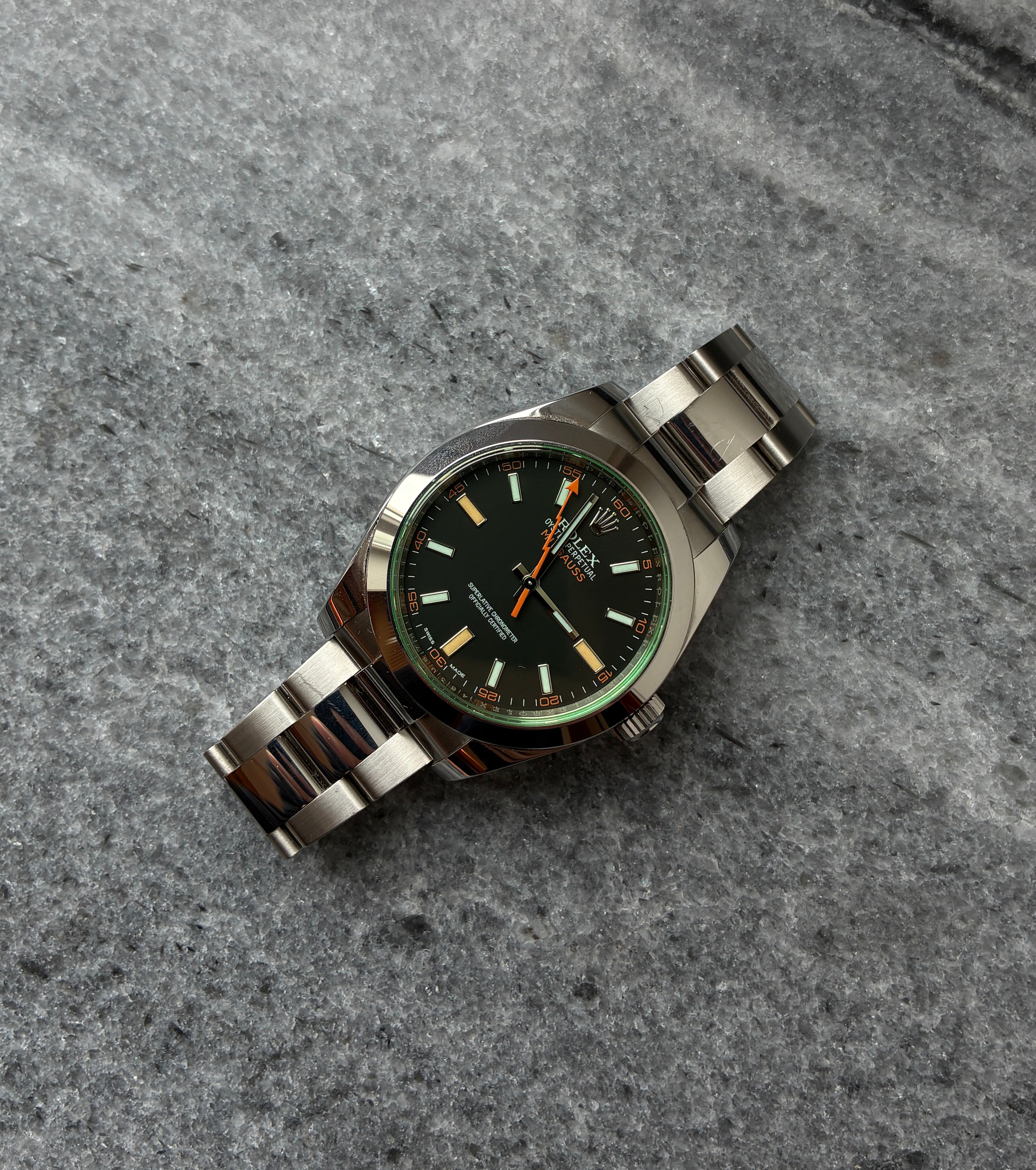 Rolex Milgauss mit schwarzem Zifferblatt und Edelstahlarmband, von oben aufgenommen auf grauem Steinboden