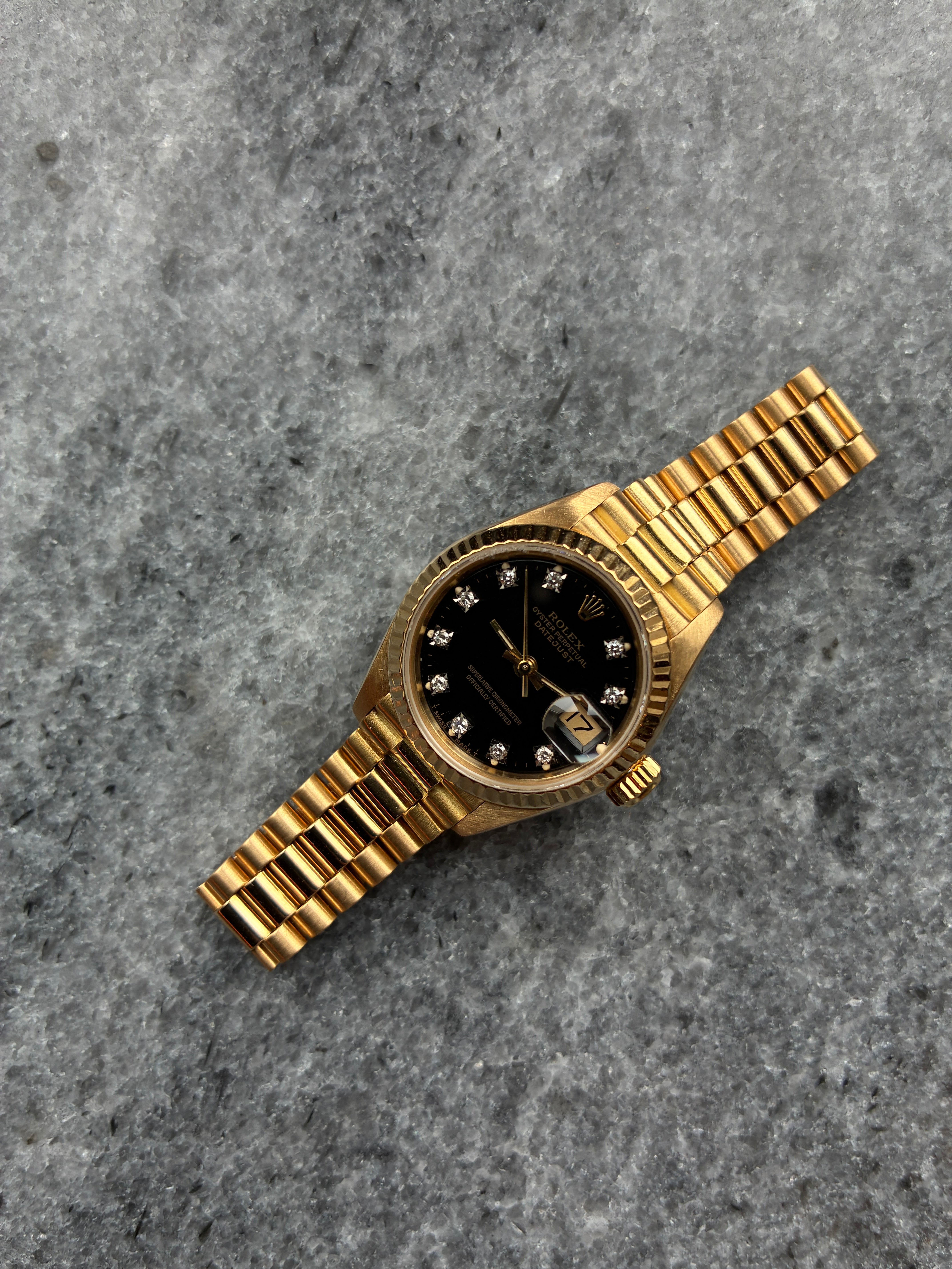 Rolex Lady-Datejust aus Gold mit schwarzem Zifferblatt und 10 Diamanten, Ansicht von oben auf grauem Marmor