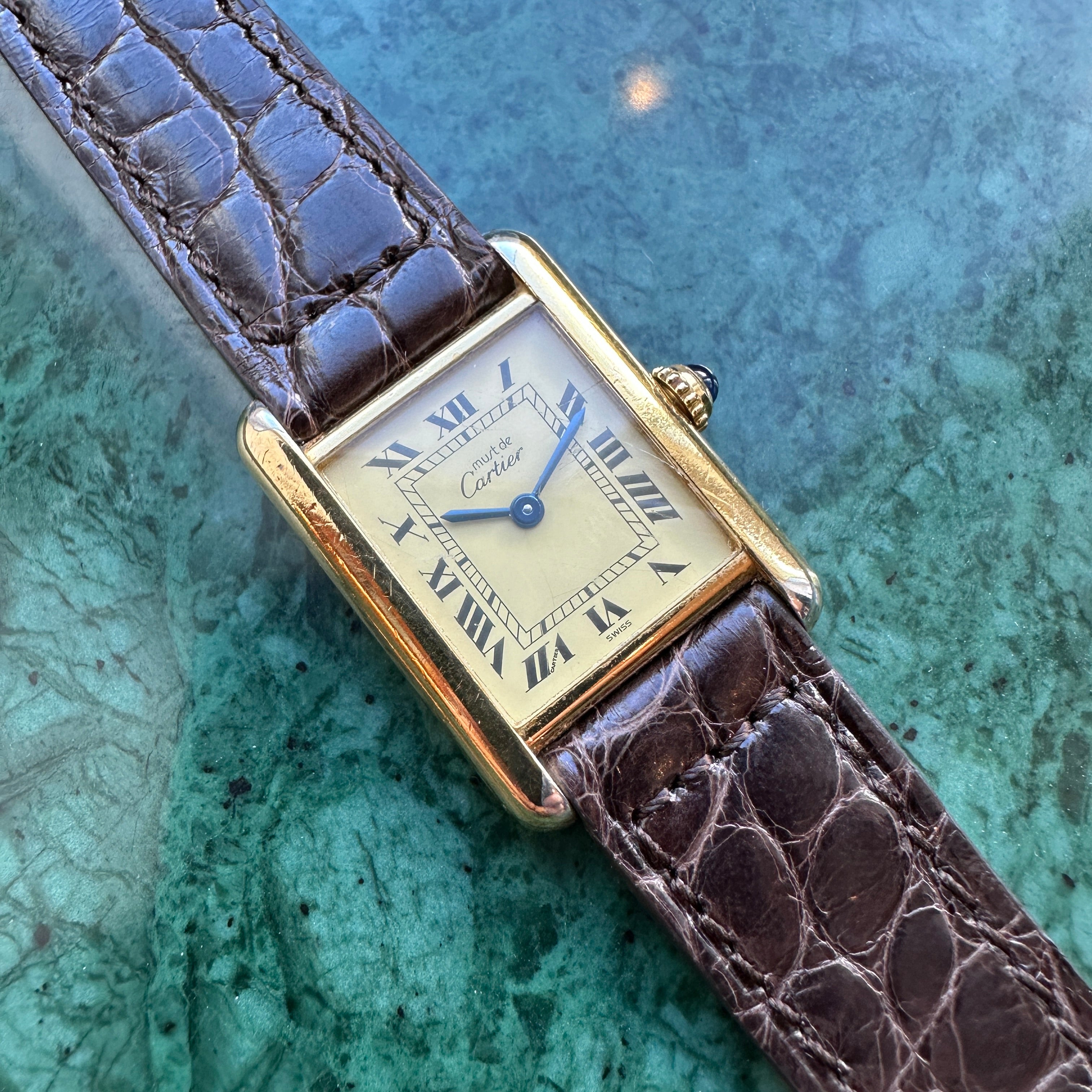 Cartier Tank Vermeil Ref. 5057001 mit braunem Krokodilarmband auf gruenem Marmor Hintergrund