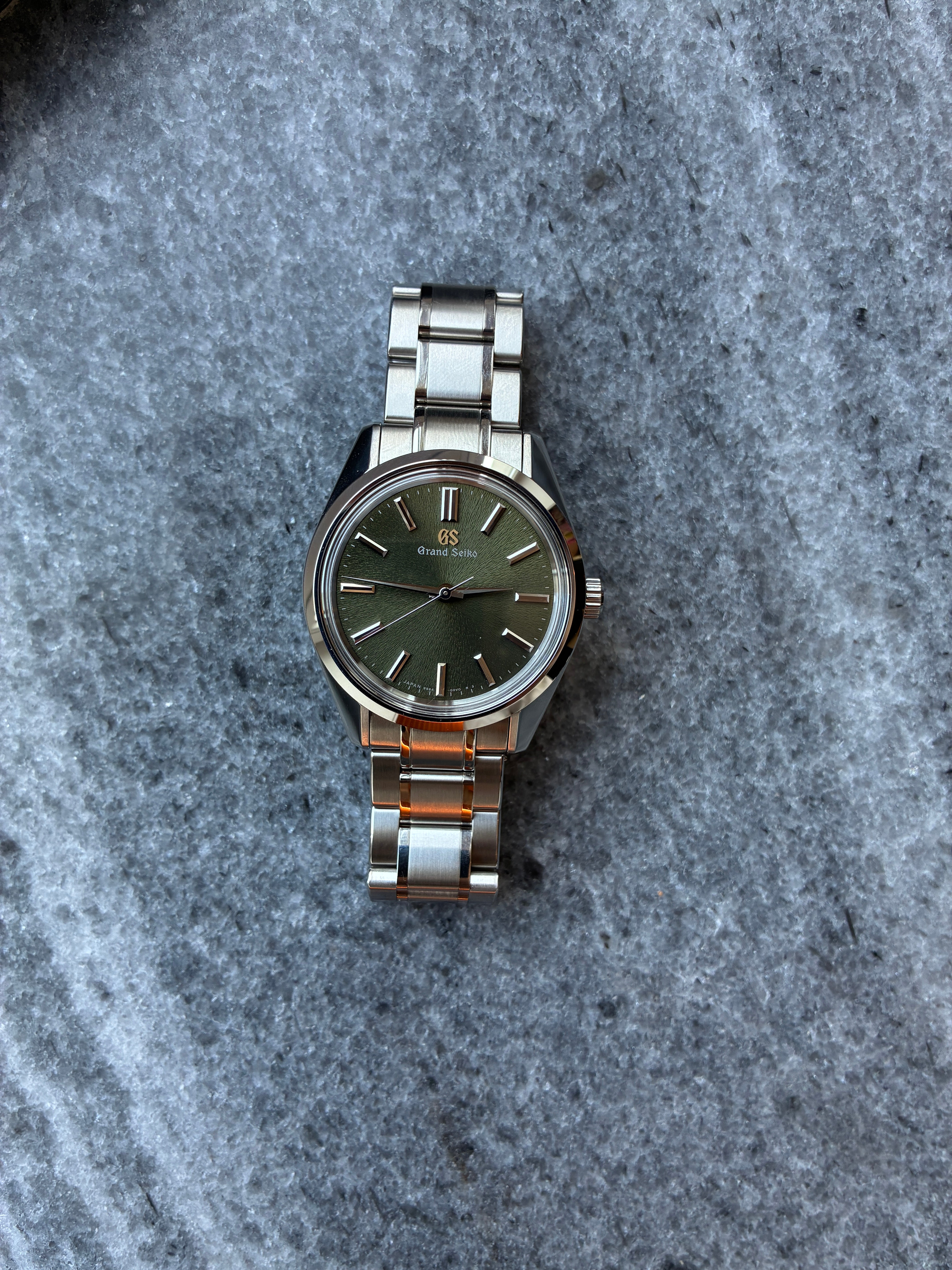 Eine Grand Seiko mit einem dunkelgrünen Zifferblatt und einem Edelstahlarmband auf einem Steinhintergrund