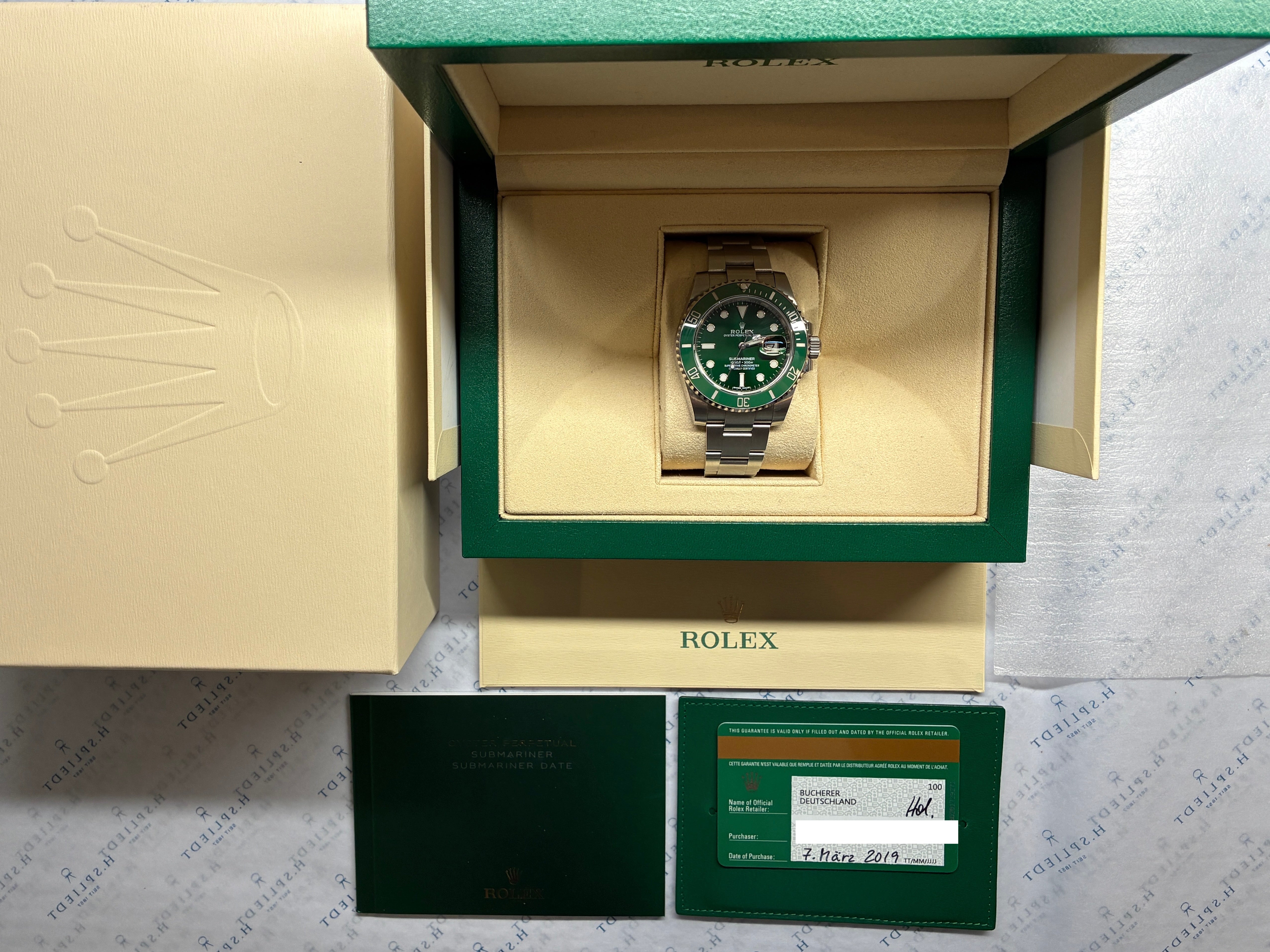 Rolex Submariner Hulk im Full-Set, Frontansicht der Uhr in geöffneter grüner Box, daneben Belege