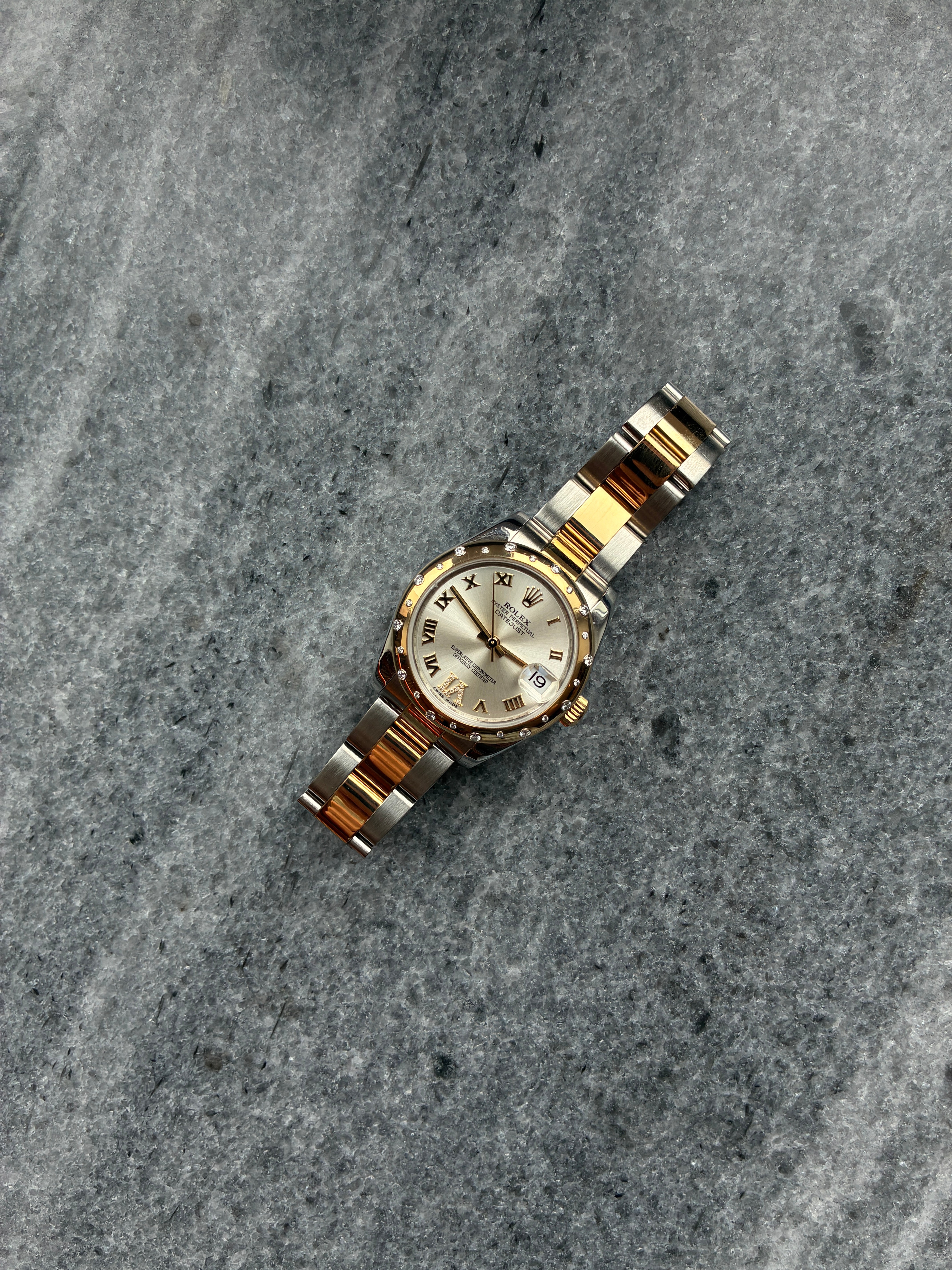 Rolex Datejust 31 in Stahl und Gold mit römischen Ziffern und Datumsanzeige auf strukturiertem Stein
