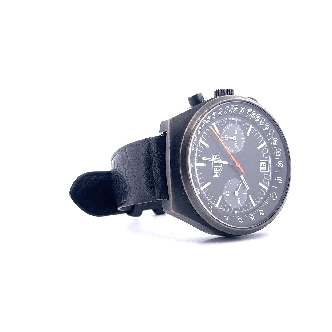 TAG Heuer Chronograph Big Shield, 1970er Jahre, schwarzes Zifferblatt, schwarzes Lederarmband, im Detail auf weißem Grund